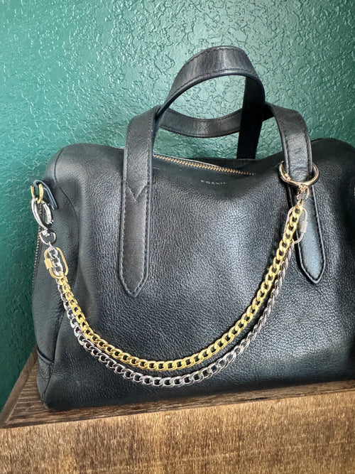 Black leather handbag with gold chain strap on a textured surface