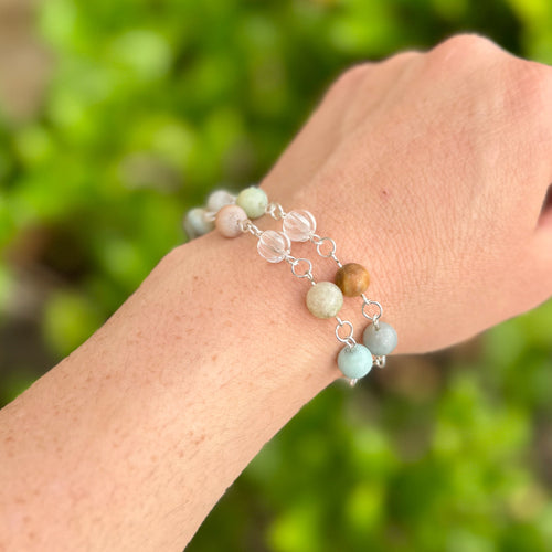 Hand wearing a amazonite bracelet against a blurred green background