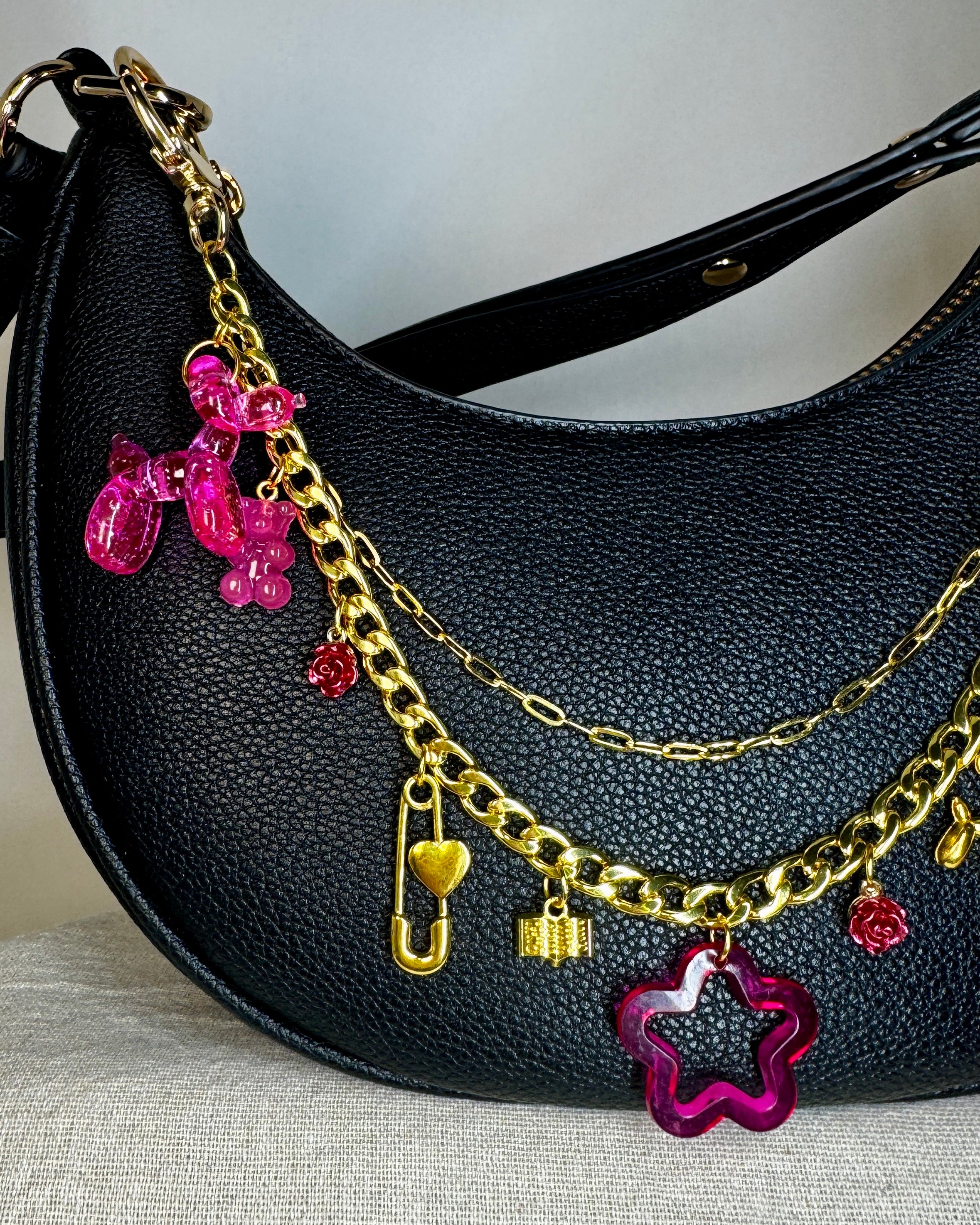 Black handbag with gold chain and colorful charms on a neutral background