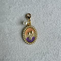 Gold charm with a purple and gold emblem on a gray textured background