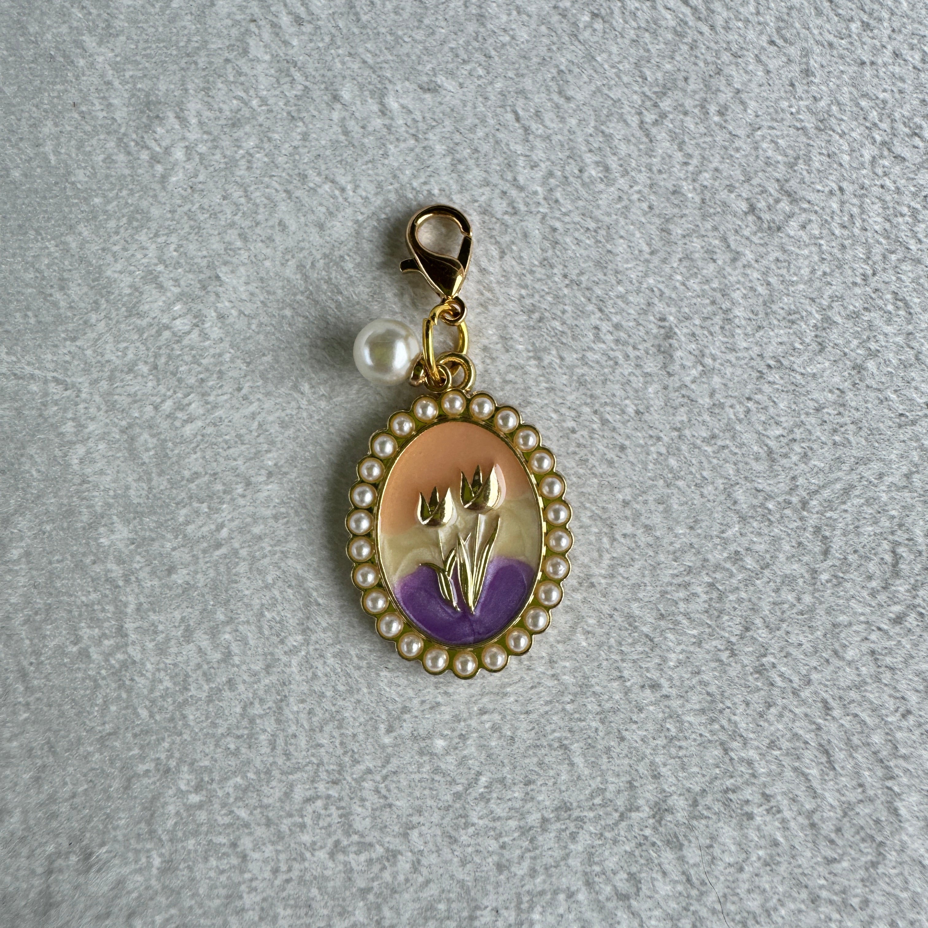 Gold charm with a purple and gold emblem on a gray textured background