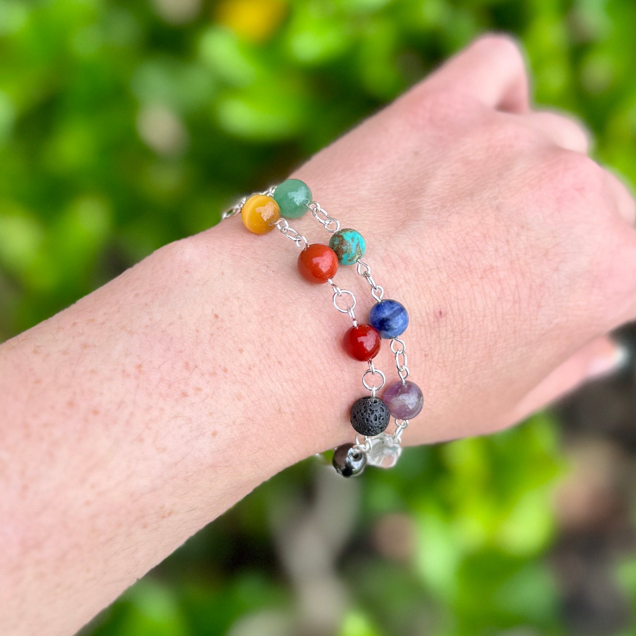 Hand wearing a chakra beaded bracelet in silver against a green leafy background