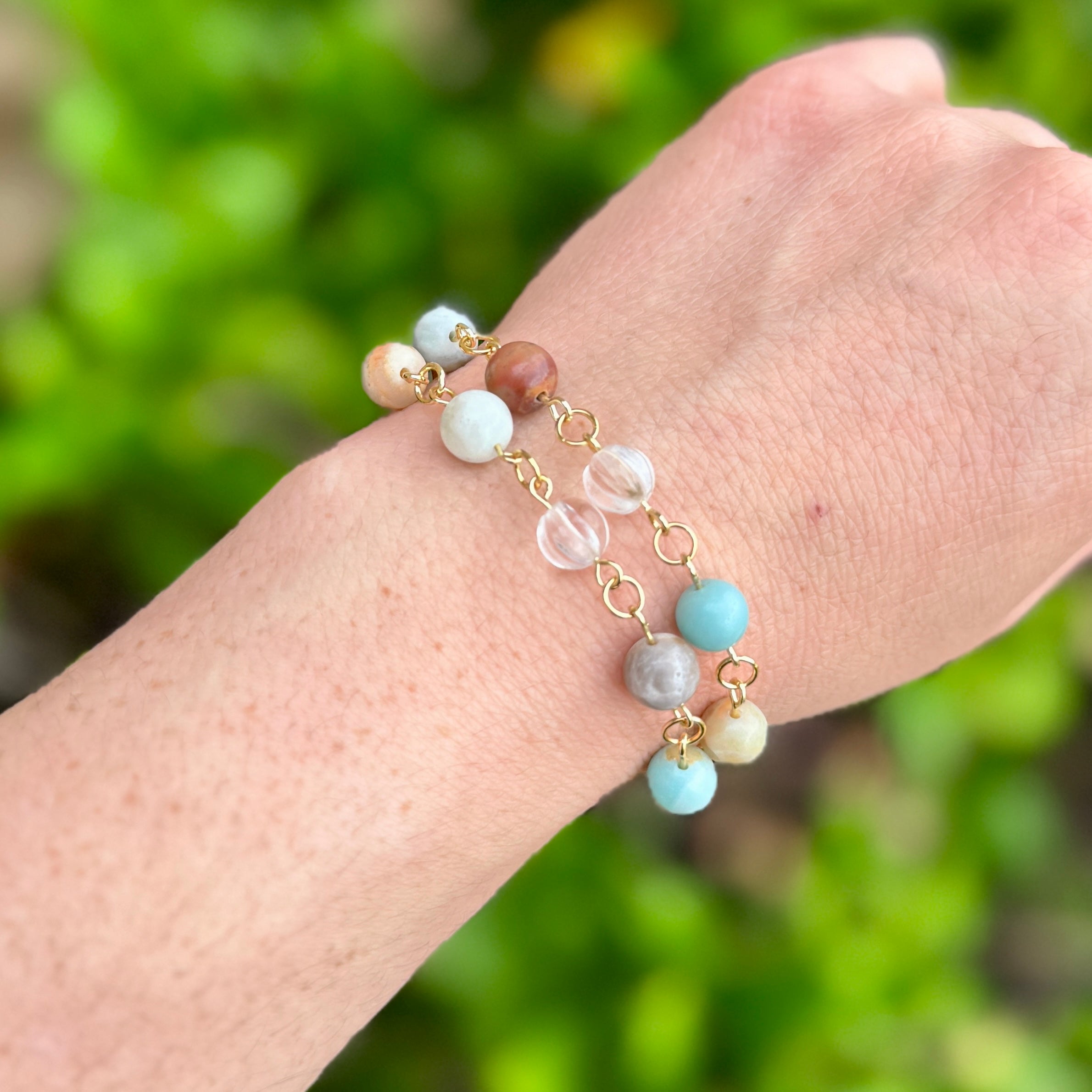 Bracelet with amazonite beaded bracelet gold on a wrist against a blurred green background