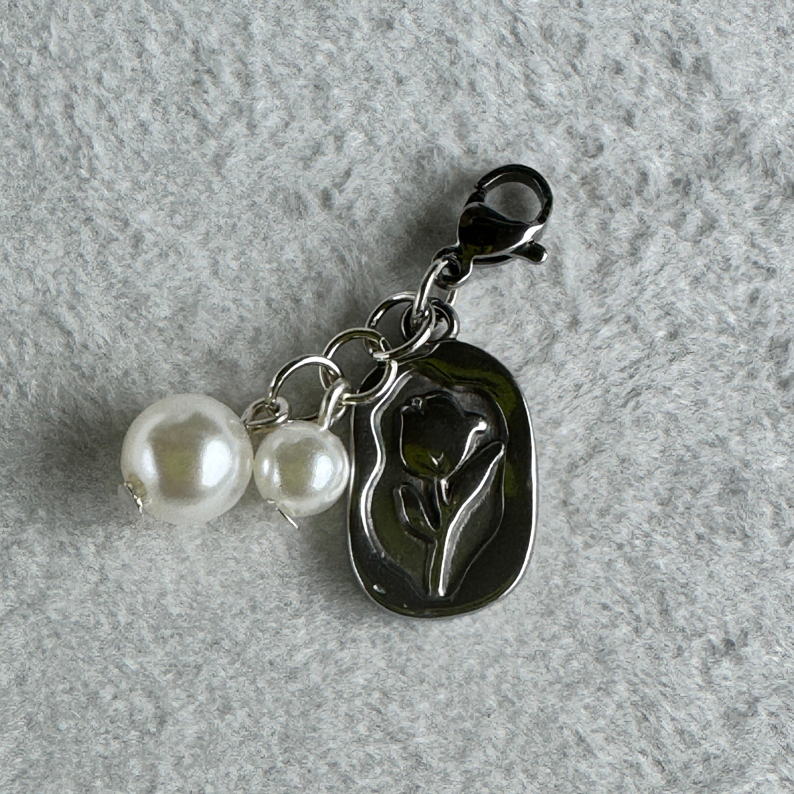 Silver charm with two pearls on a gray textured background