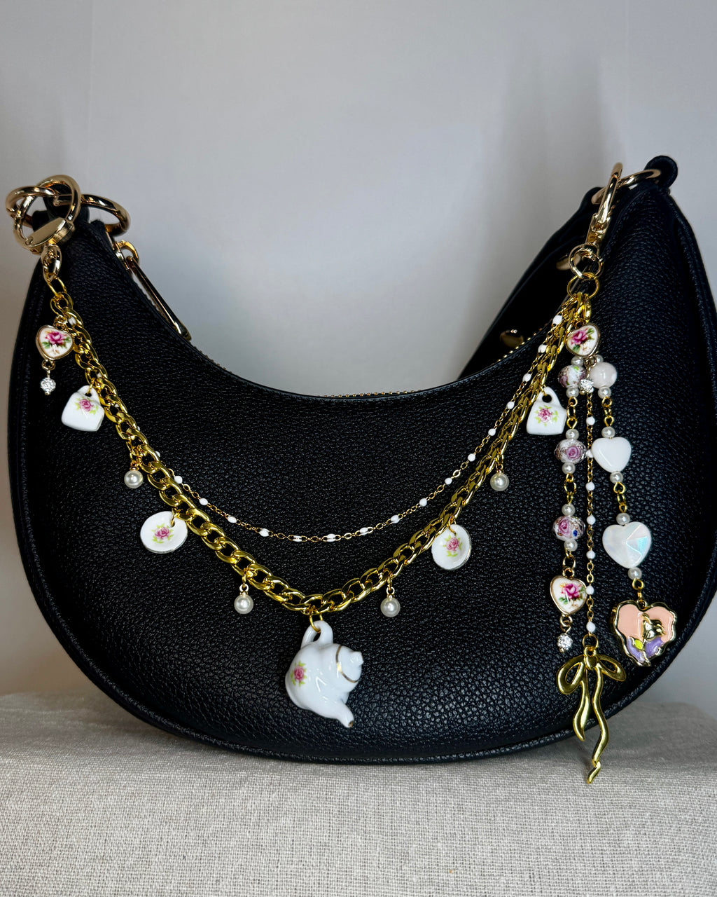 Black handbag with decorative gold chain and charms on a neutral background