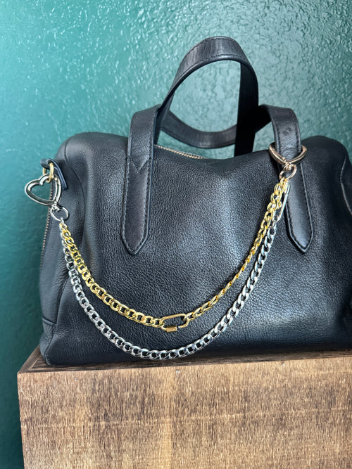 Black leather handbag with gold and silver chains on a teal surface
