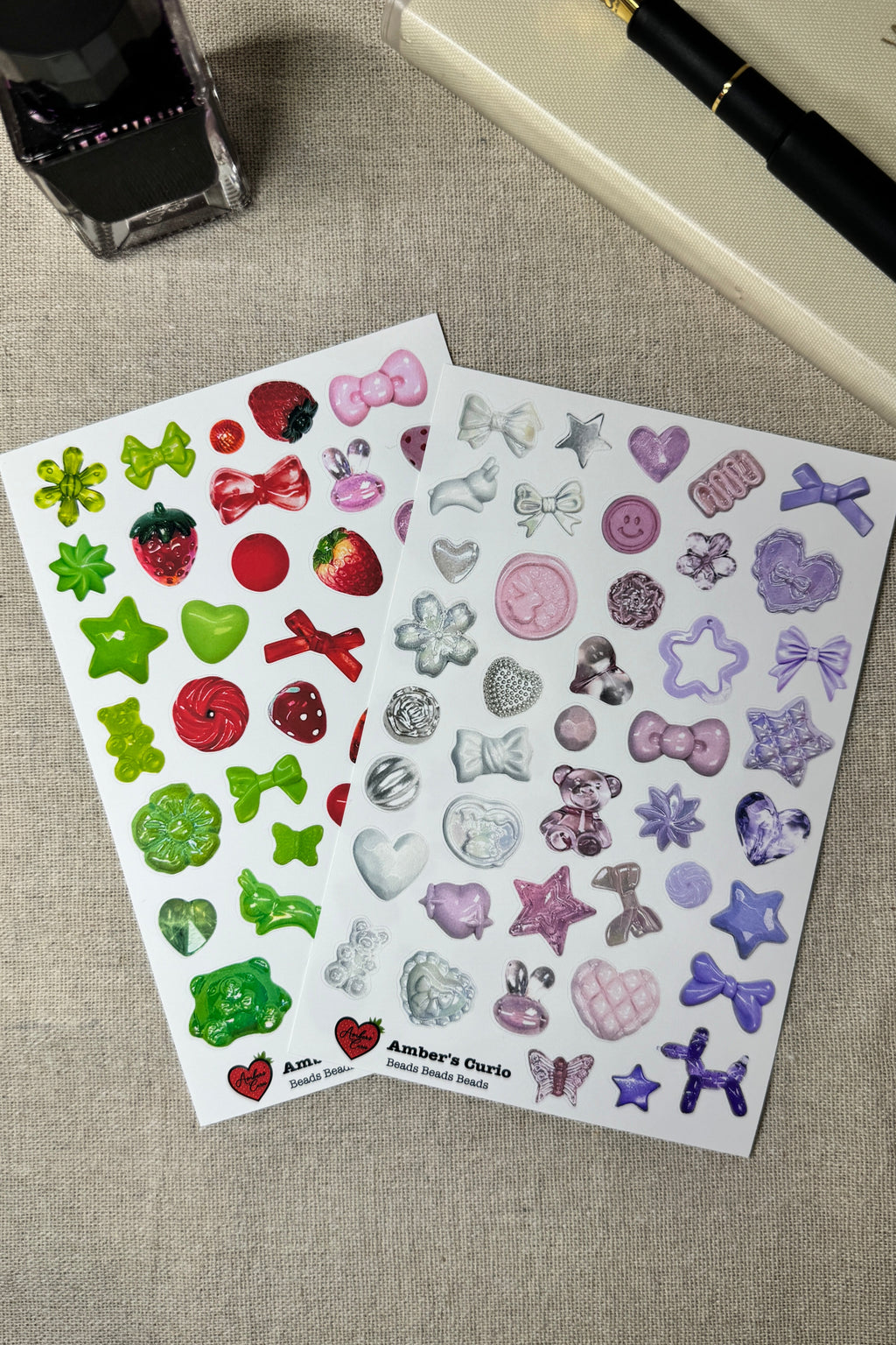 Two sheets of decorative stickers featuring beads on a textured surface with a pen and ink bottle.