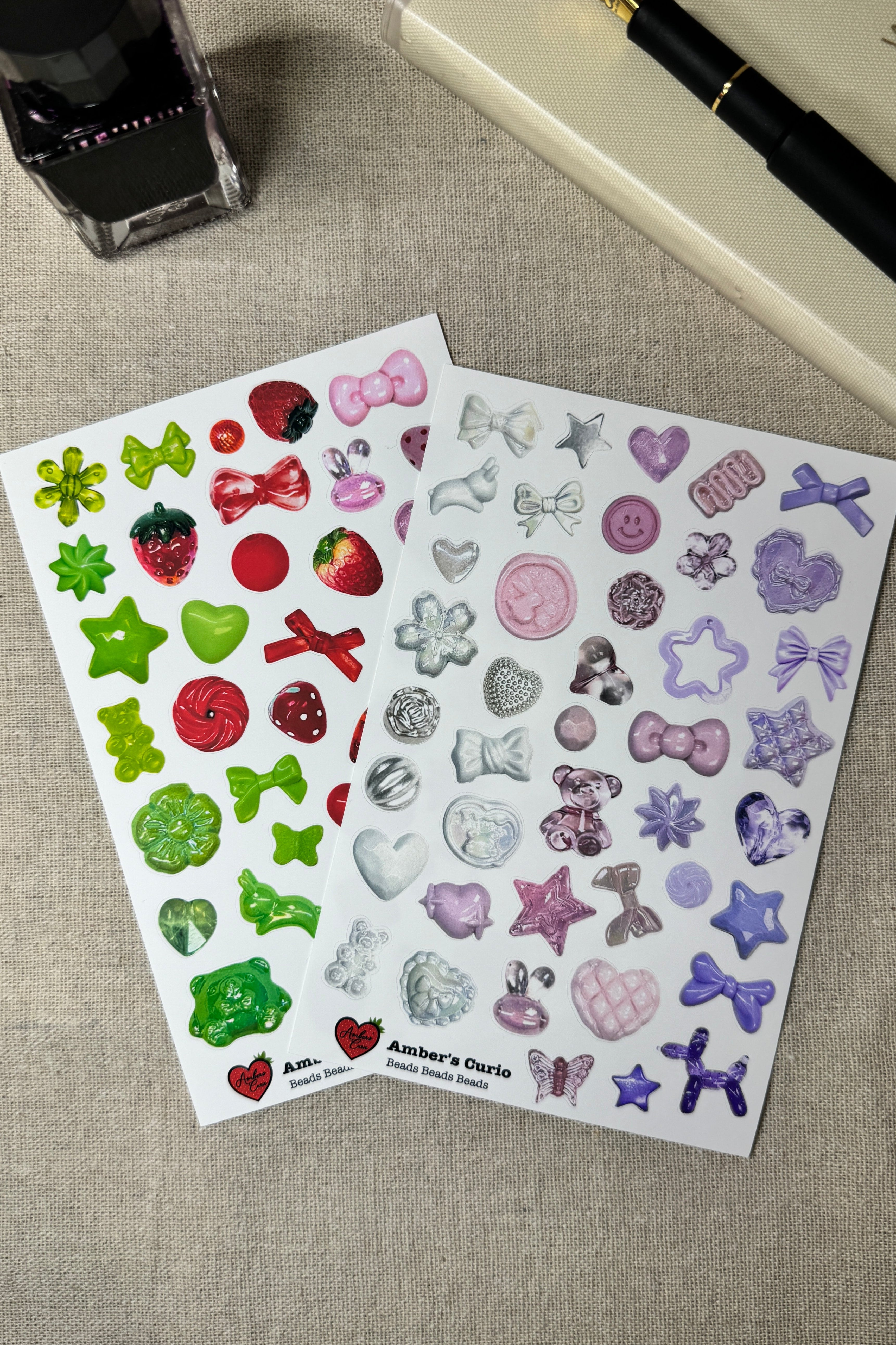 Two sheets of decorative stickers featuring beads on a textured surface with a pen and ink bottle.