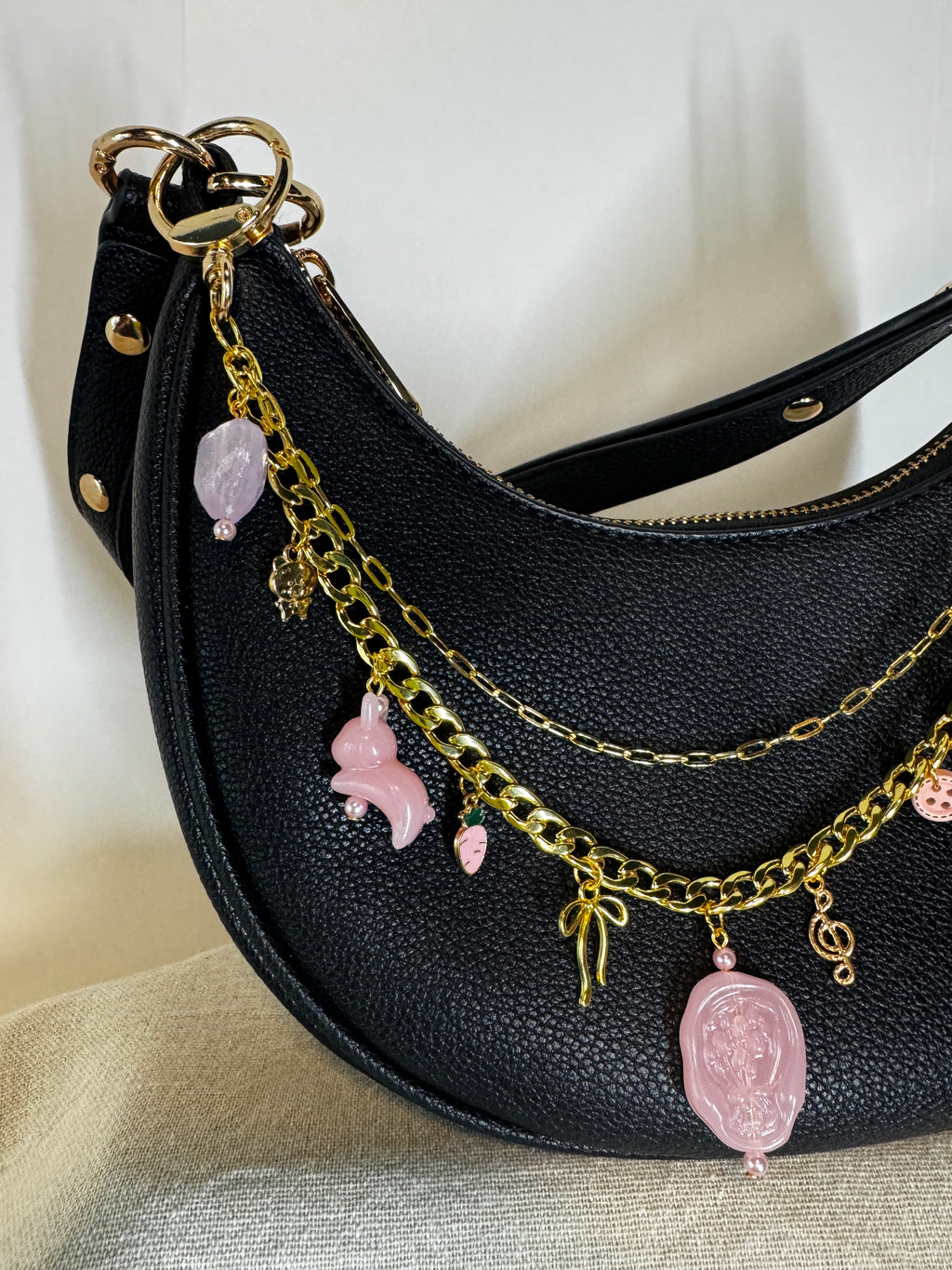 Black handbag with gold chain and pink charms on a light background