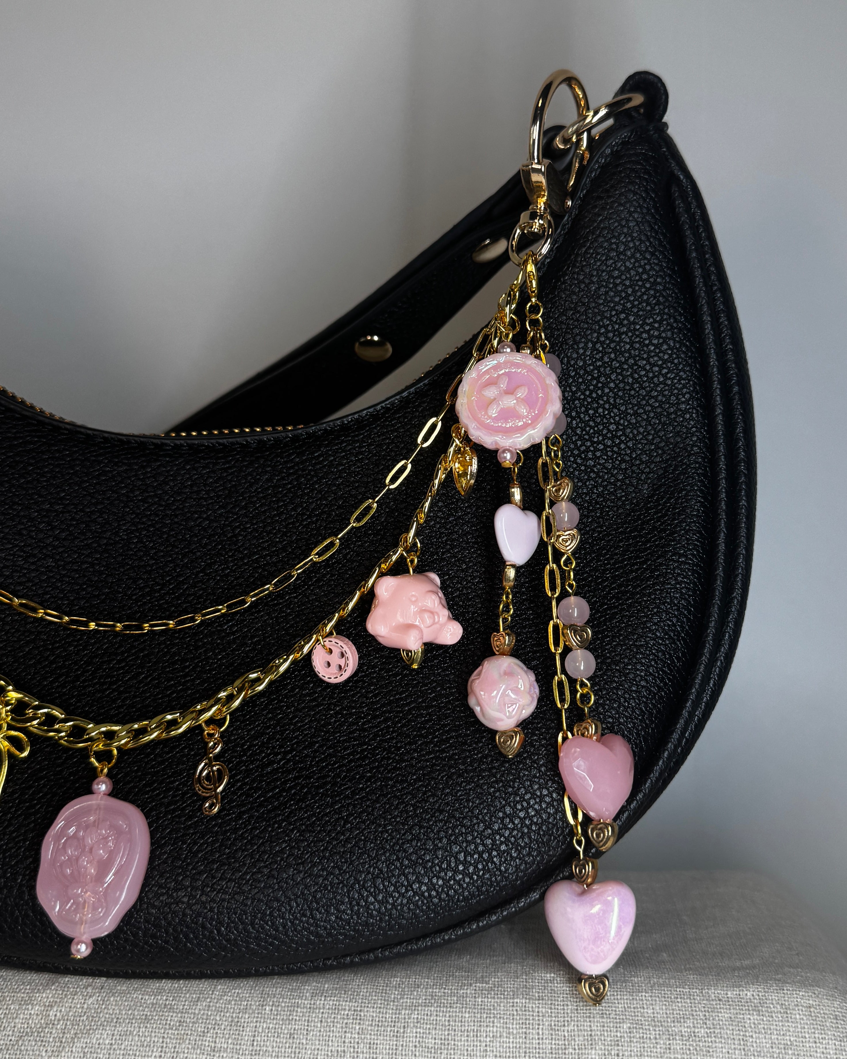 Black handbag with pink charm chain on a gray surface