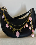 Black handbag with gold and pink charm strap on a neutral background