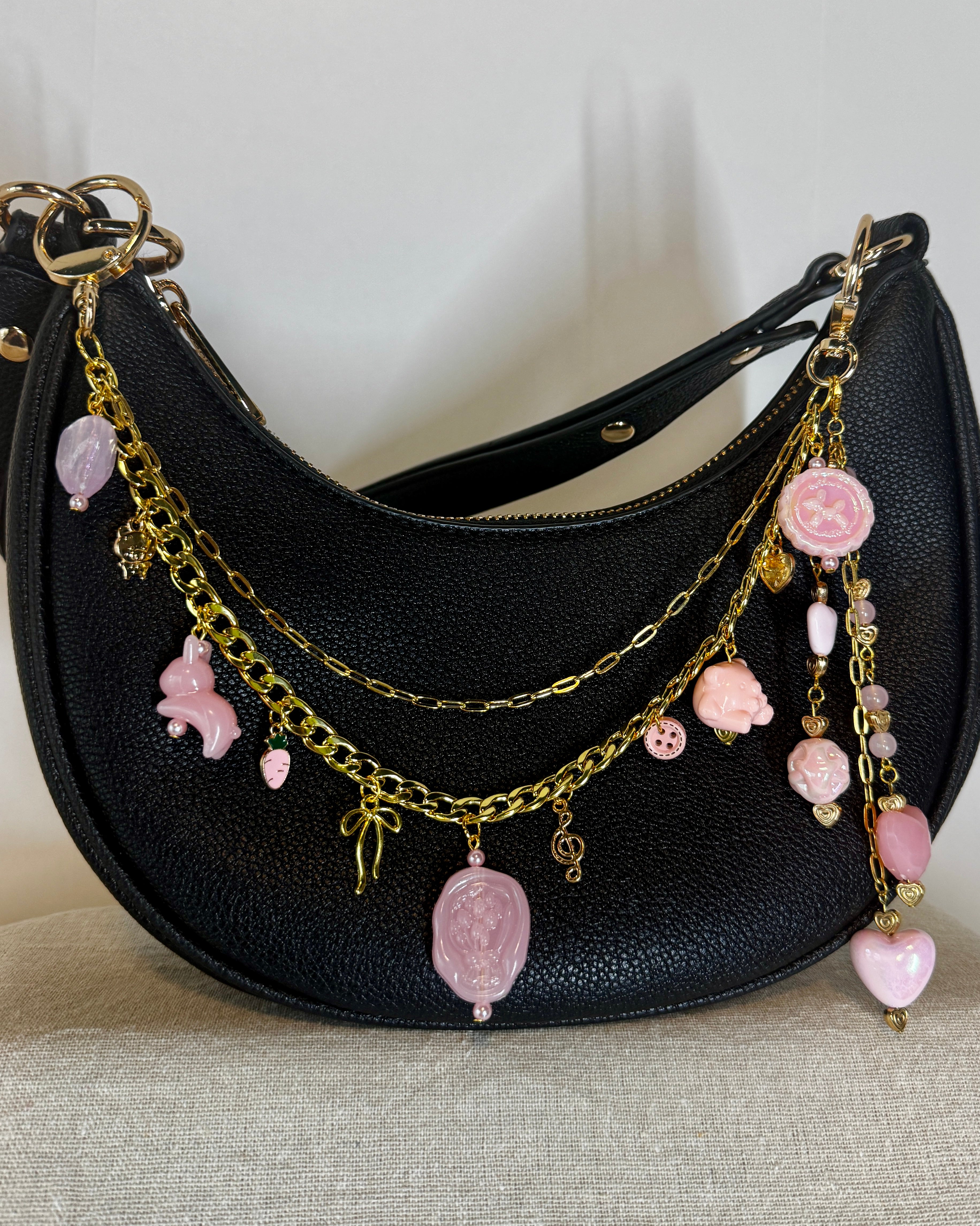 Black handbag with gold and pink charm strap on a neutral background