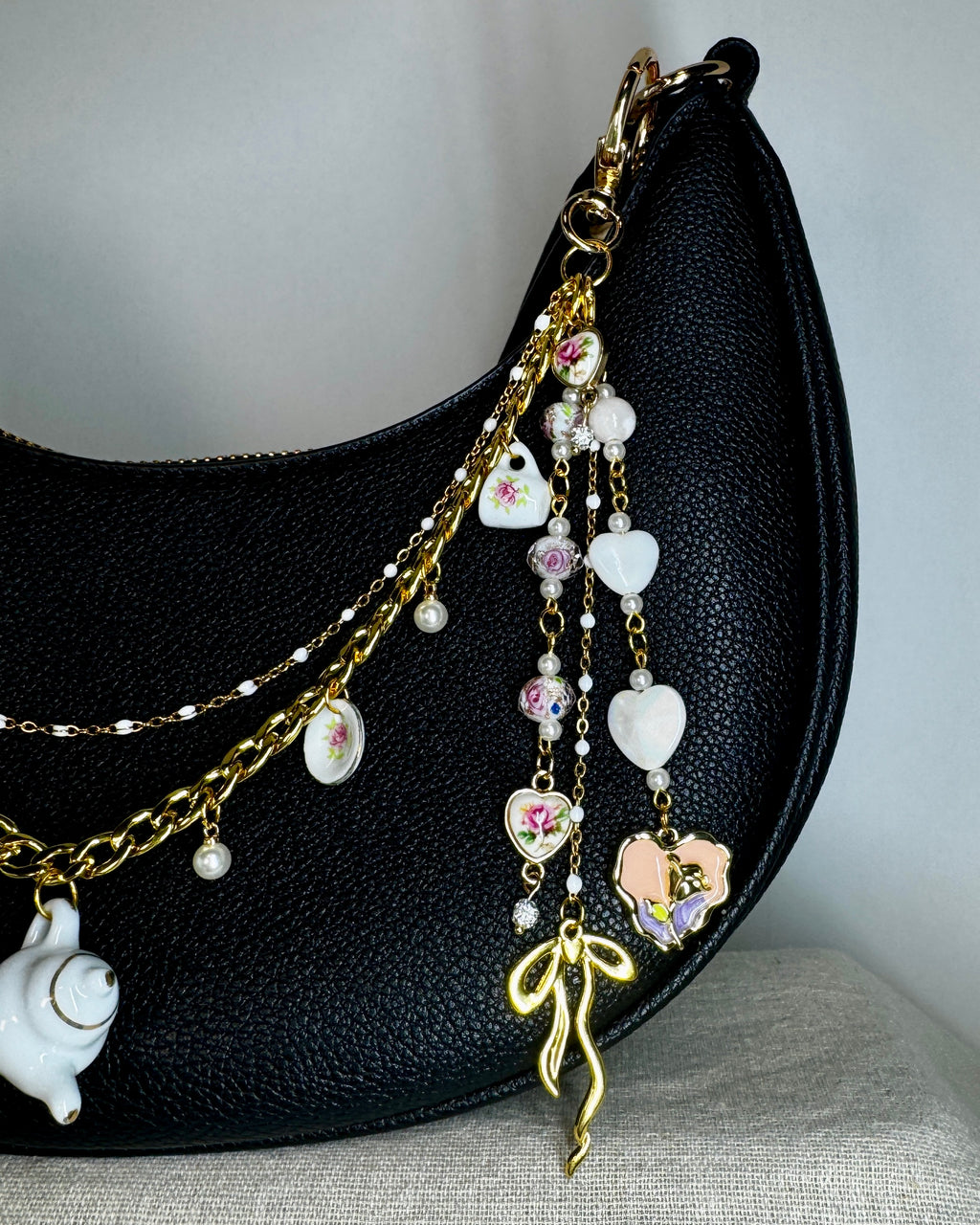 Black handbag with decorative charm featuring white and gold elements on a neutral background