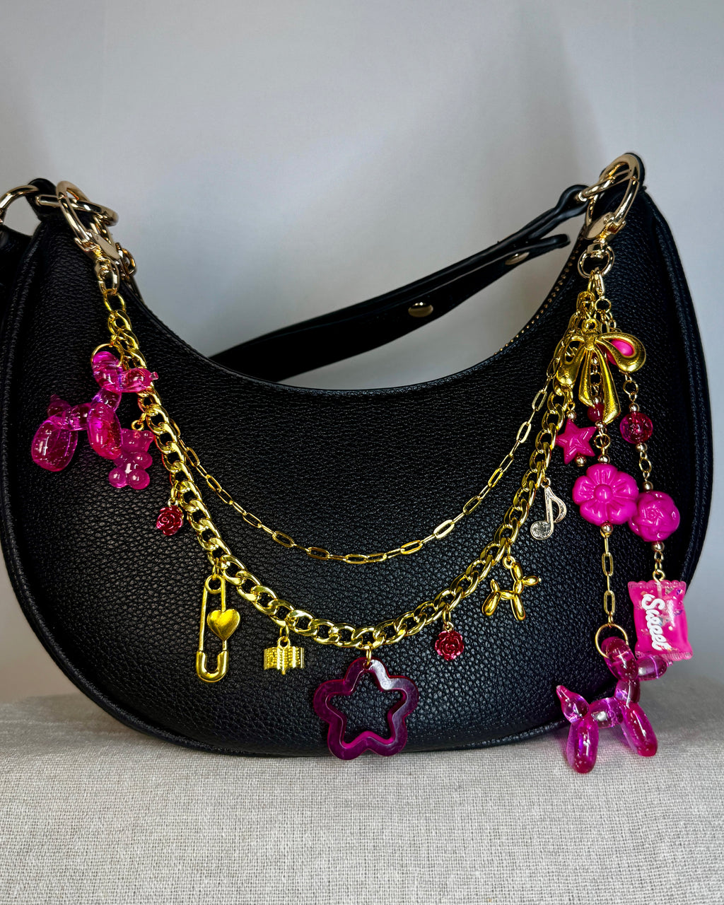 Black handbag with gold and pink charms on a light gray background