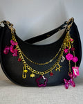 Black handbag with gold and pink charms on a light gray background