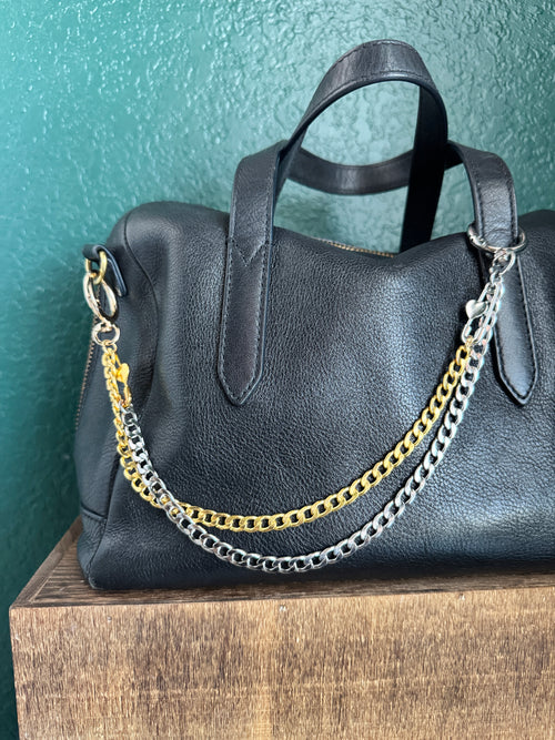 Black leather bag with gold and silver chain strap on a green surface