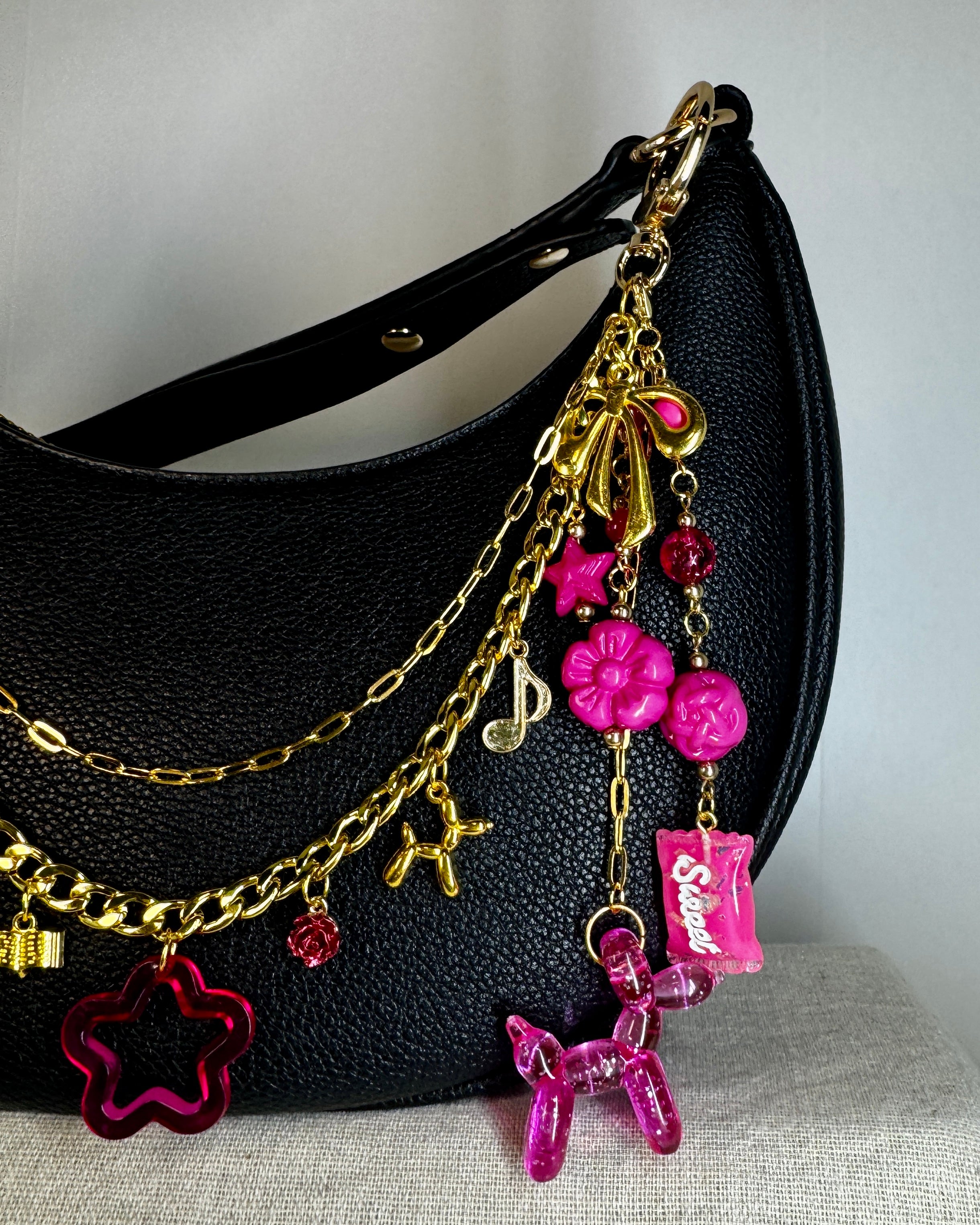 Black handbag with gold chain and pink charms on a neutral background