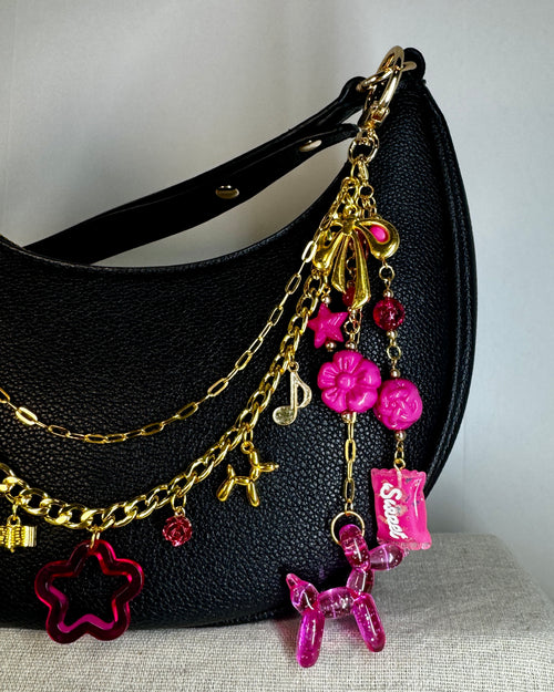 Black handbag with gold chain and pink charms on a neutral background