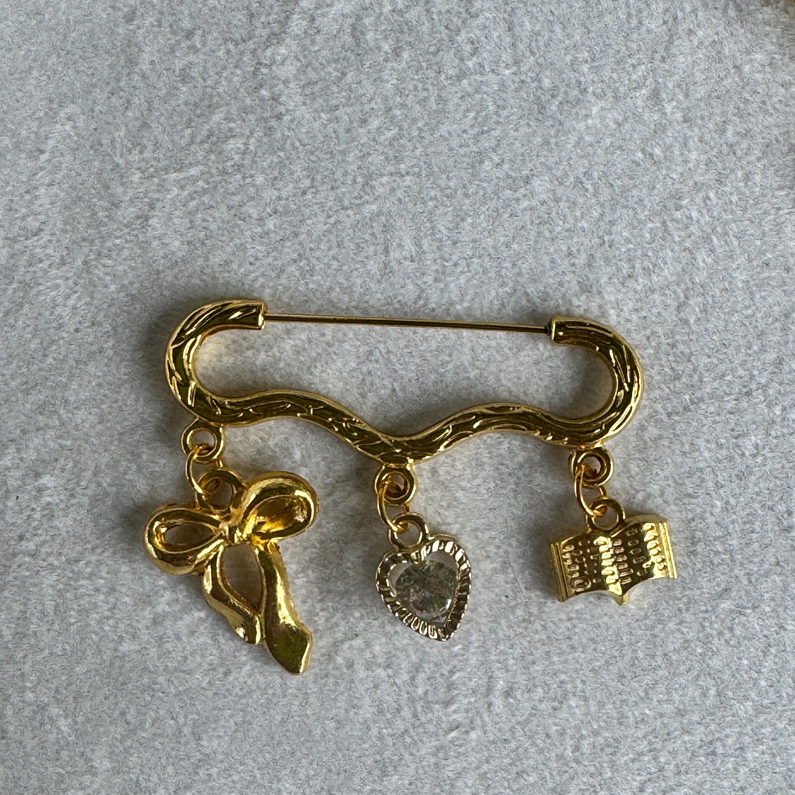 Gold safety pin brooch with decorative elements on a light gray background