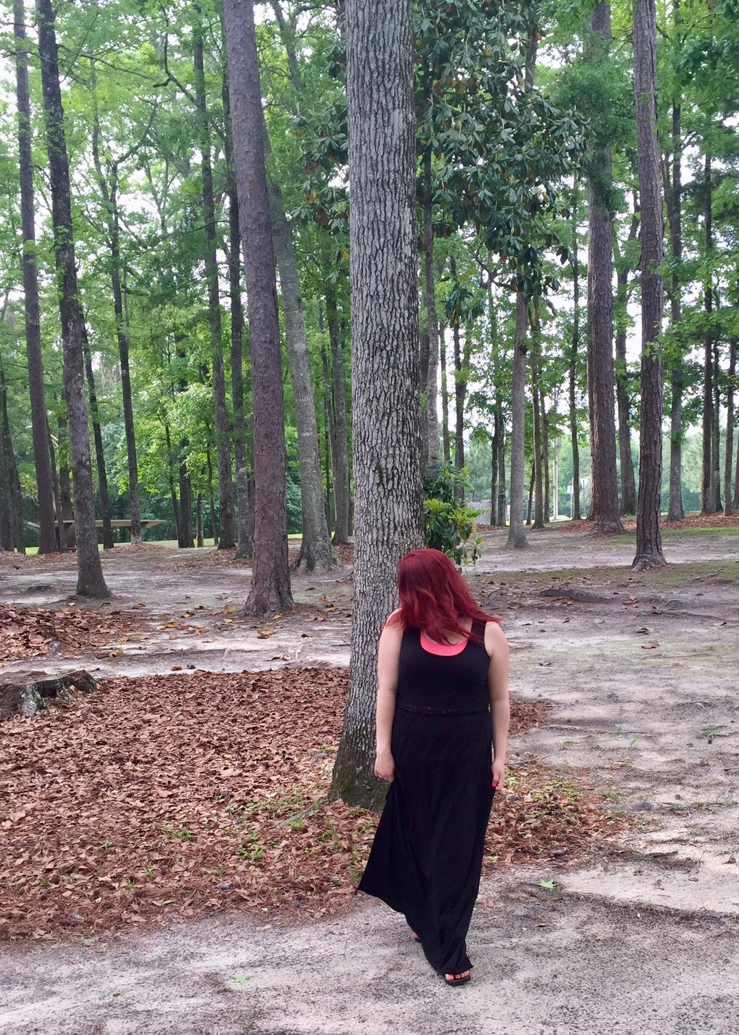 Person standing in a wooded park, facing trees, symbolizing grounding and  nature. 