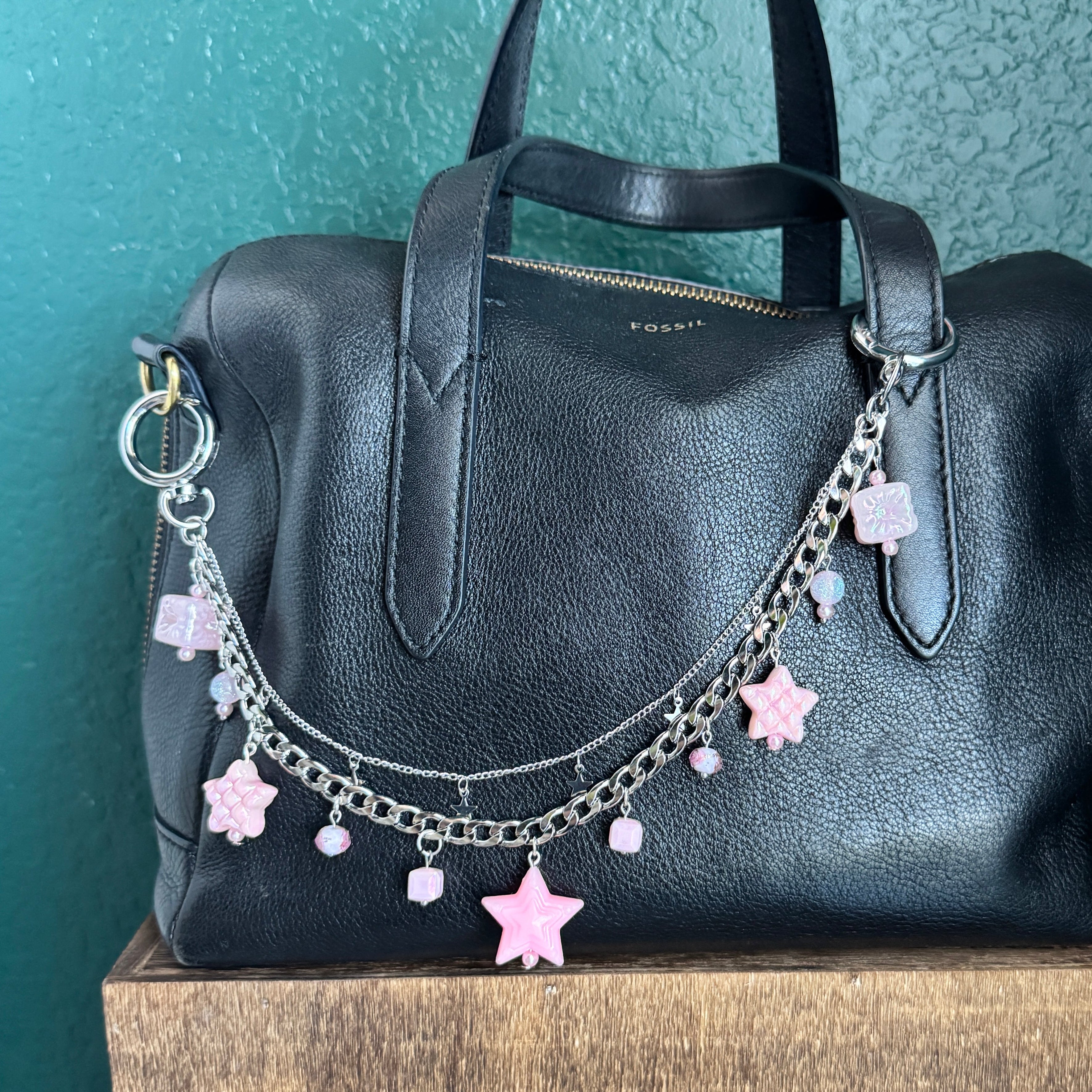 Black handbag with decorative chain and stars on a teal surface