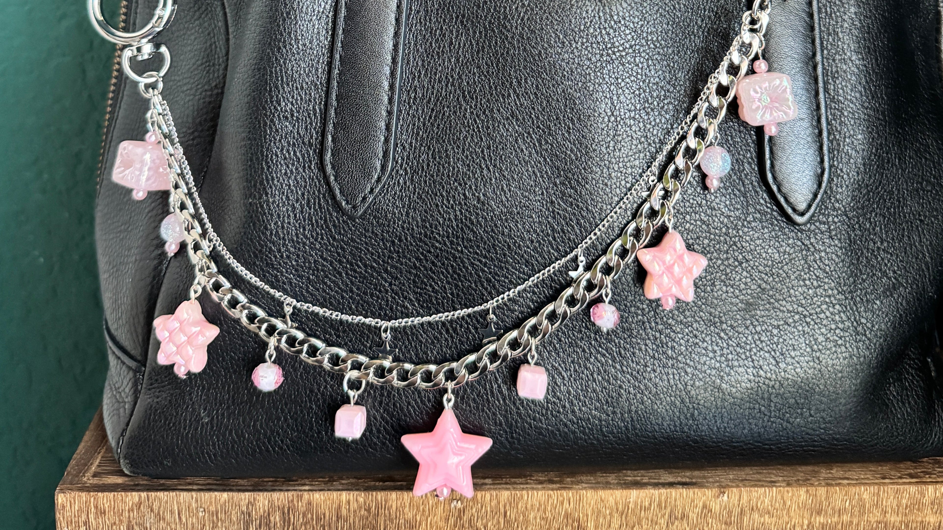 Black leather bag with decorative pink star charm on a textured green surface