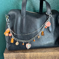 Black leather handbag with colorful charm chain on a teal surface