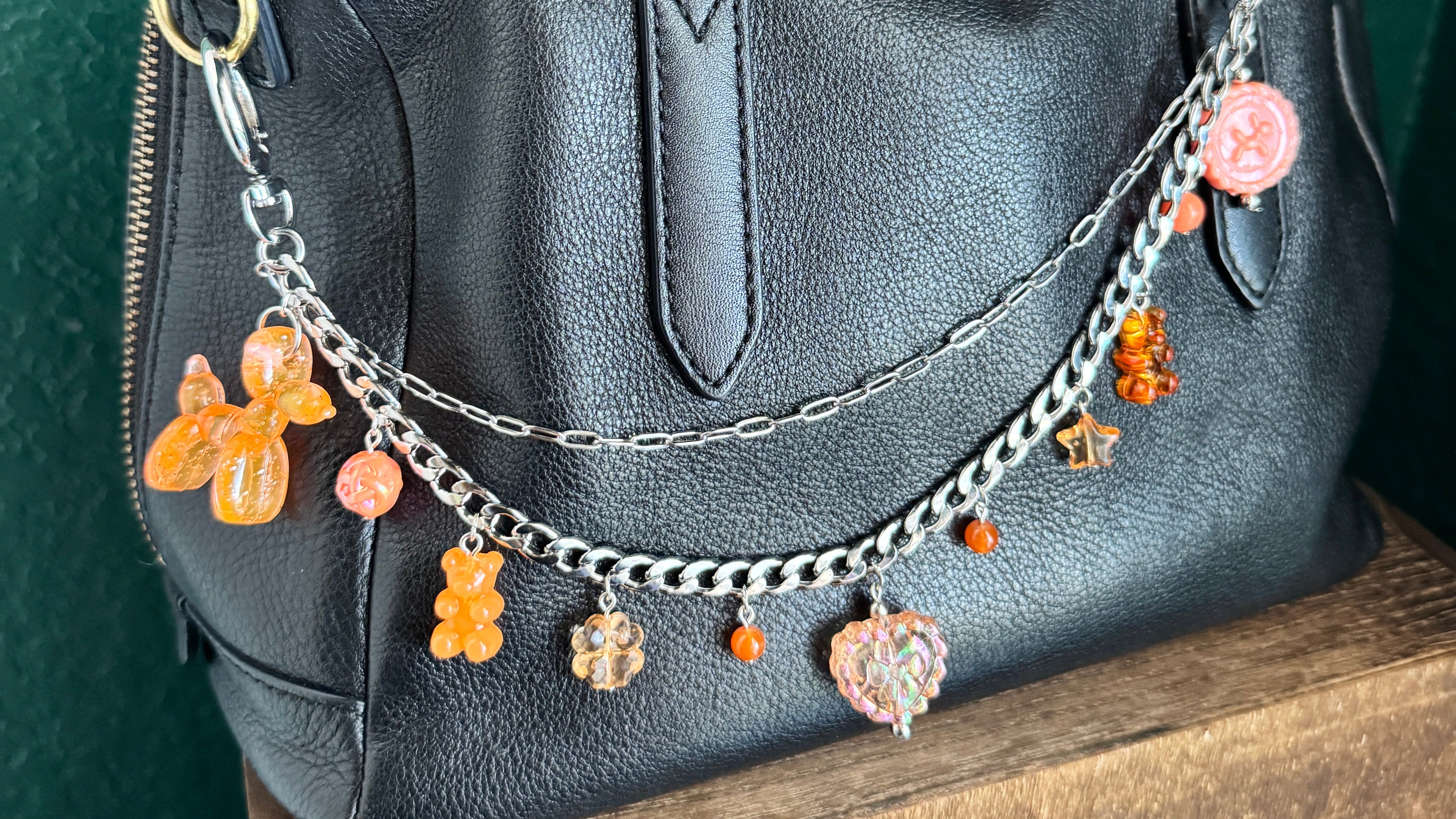 Black leather handbag with decorative chain and charms on a textured surface