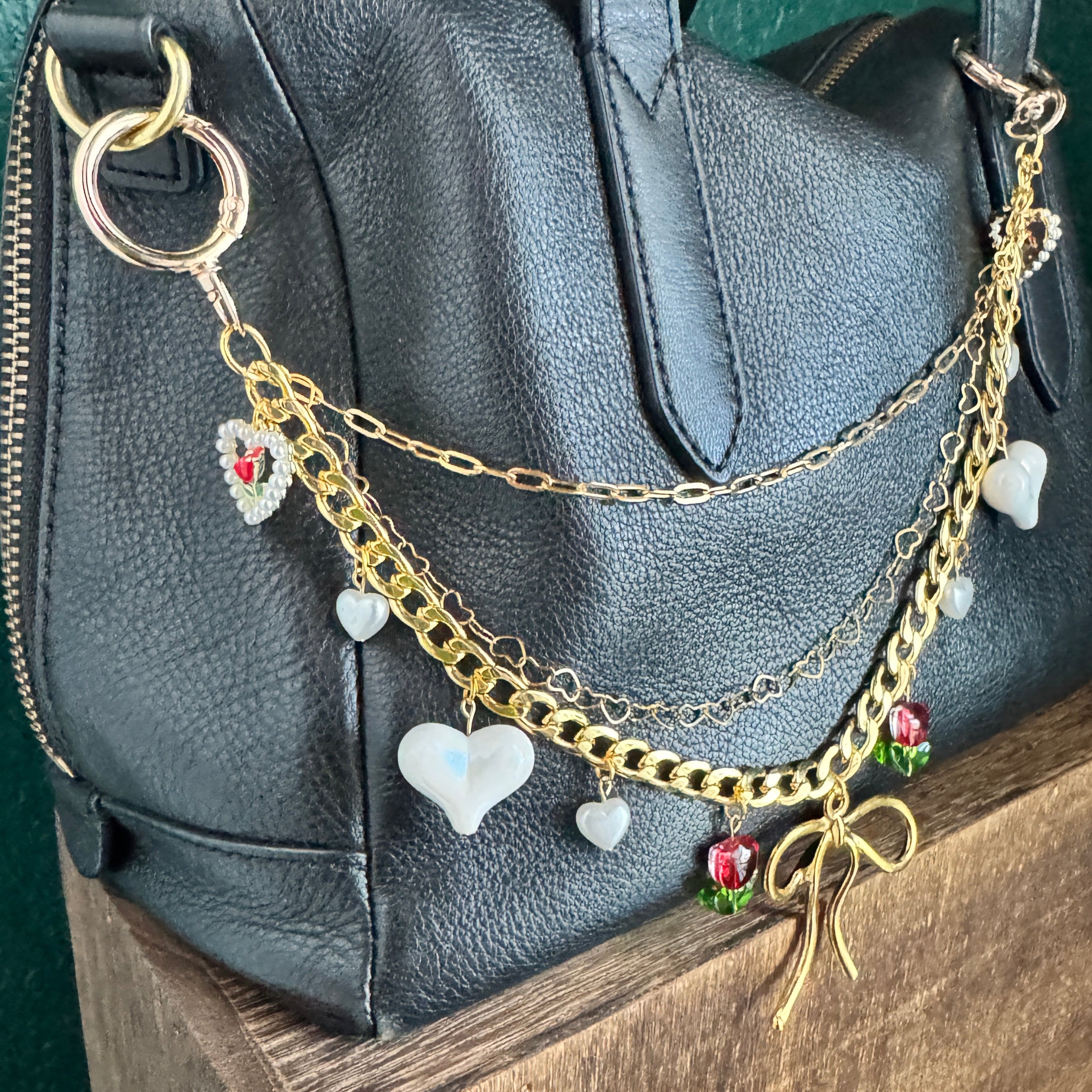 Gold chain with charms draped over a black leather bag on a wooden surface.