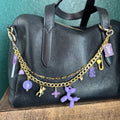 Black handbag with gold chain and purple charms on a wooden surface