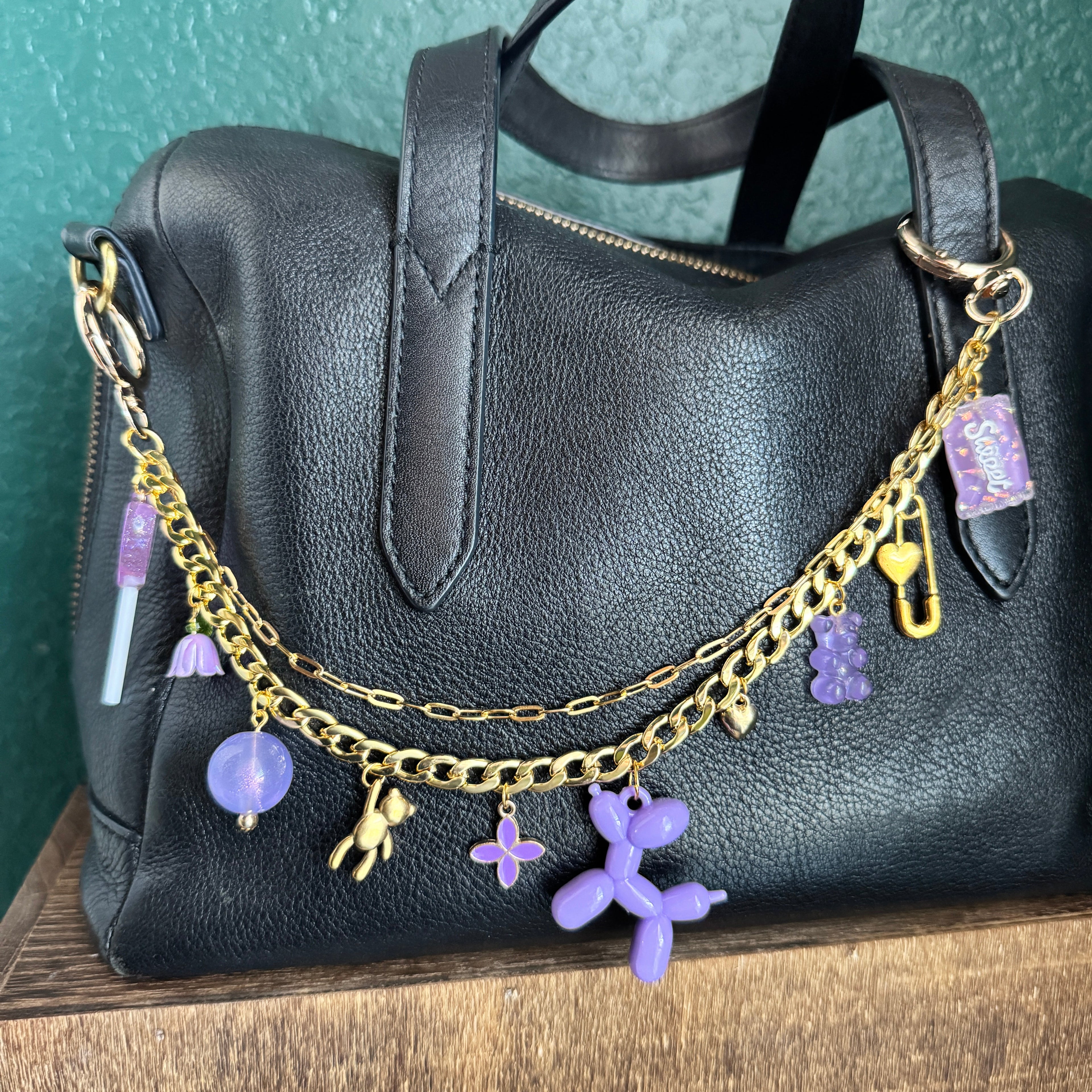 Black handbag with gold chain and purple charms on a wooden surface
