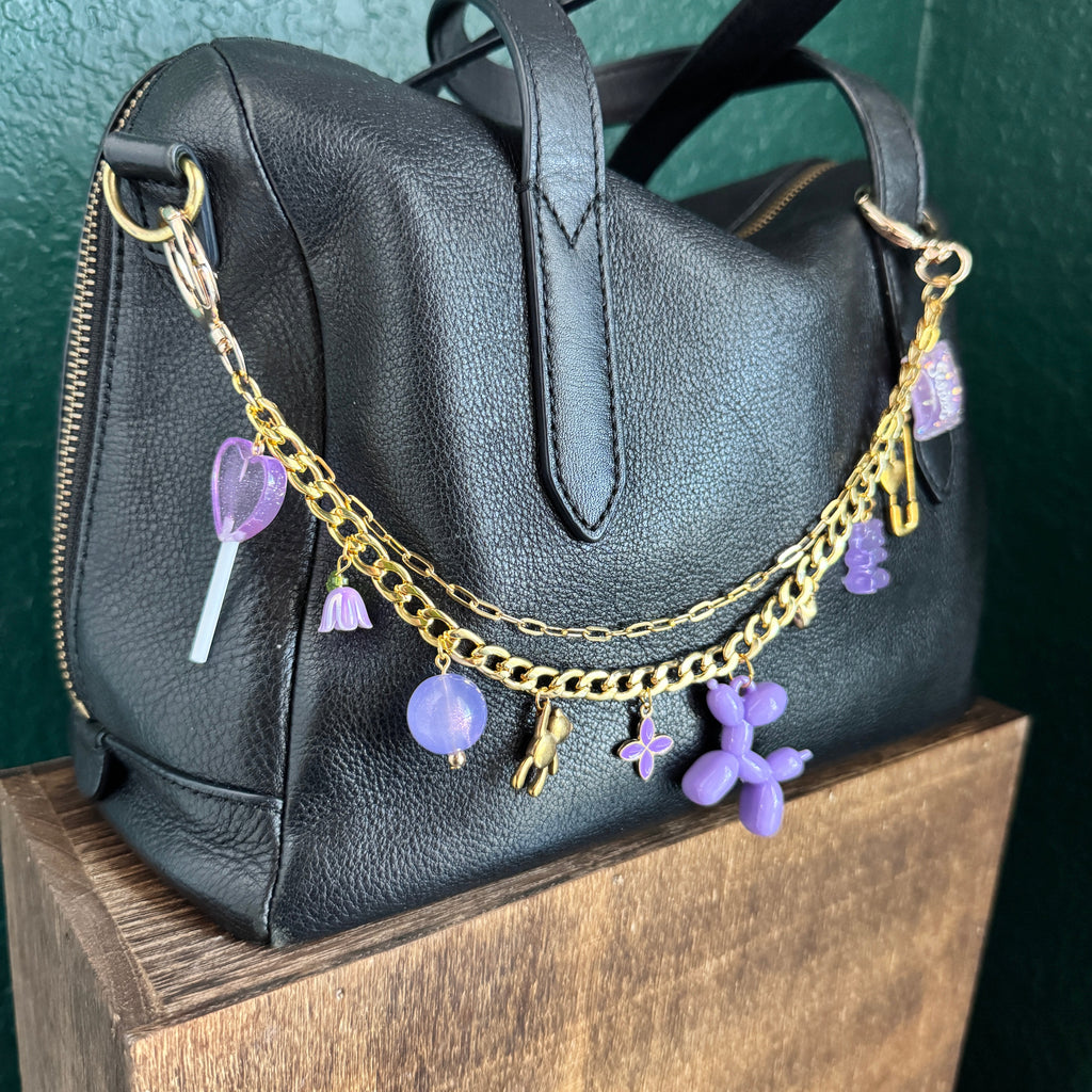Black backpack with gold chain and purple charms on a green surface