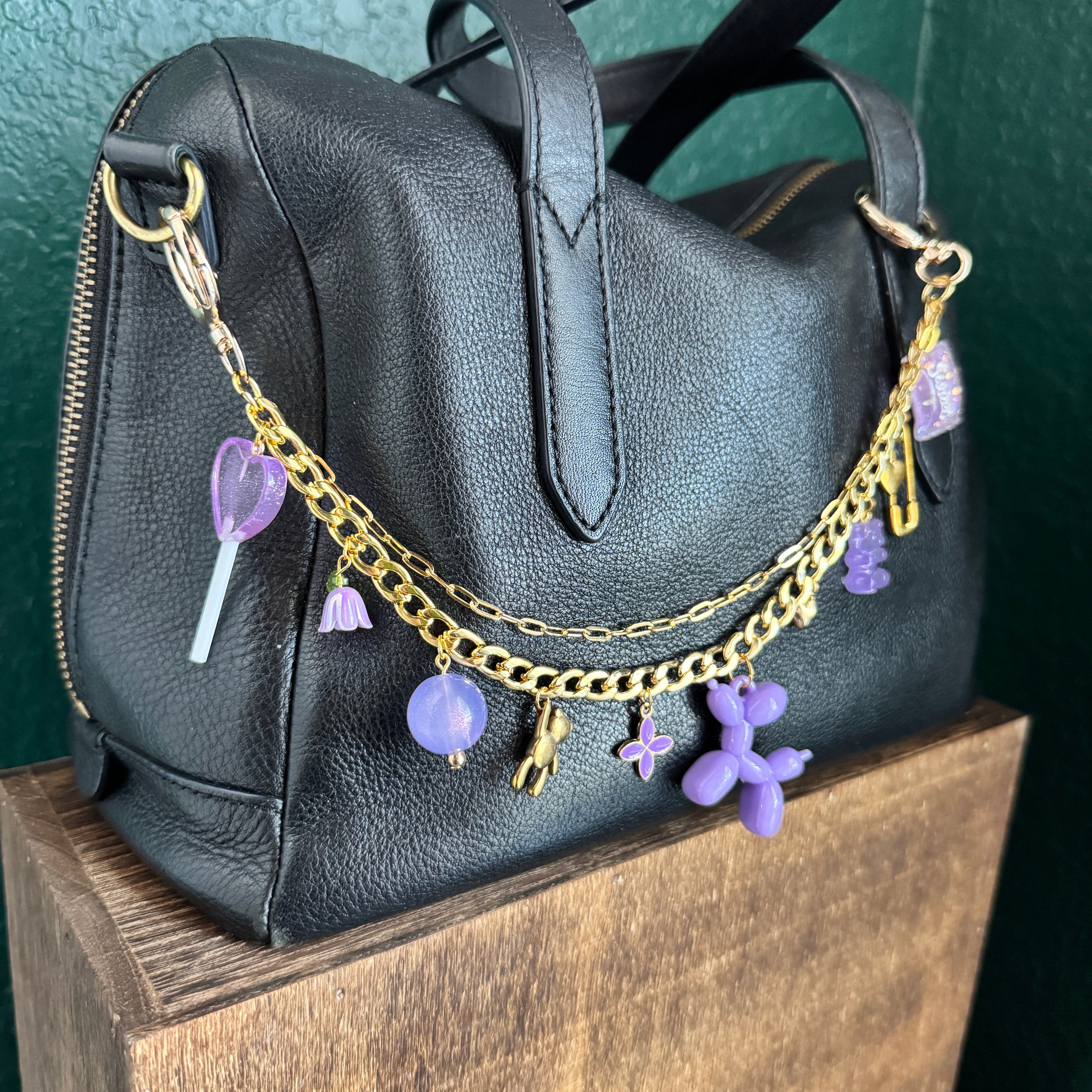 Black backpack with gold chain and purple charms on a green surface