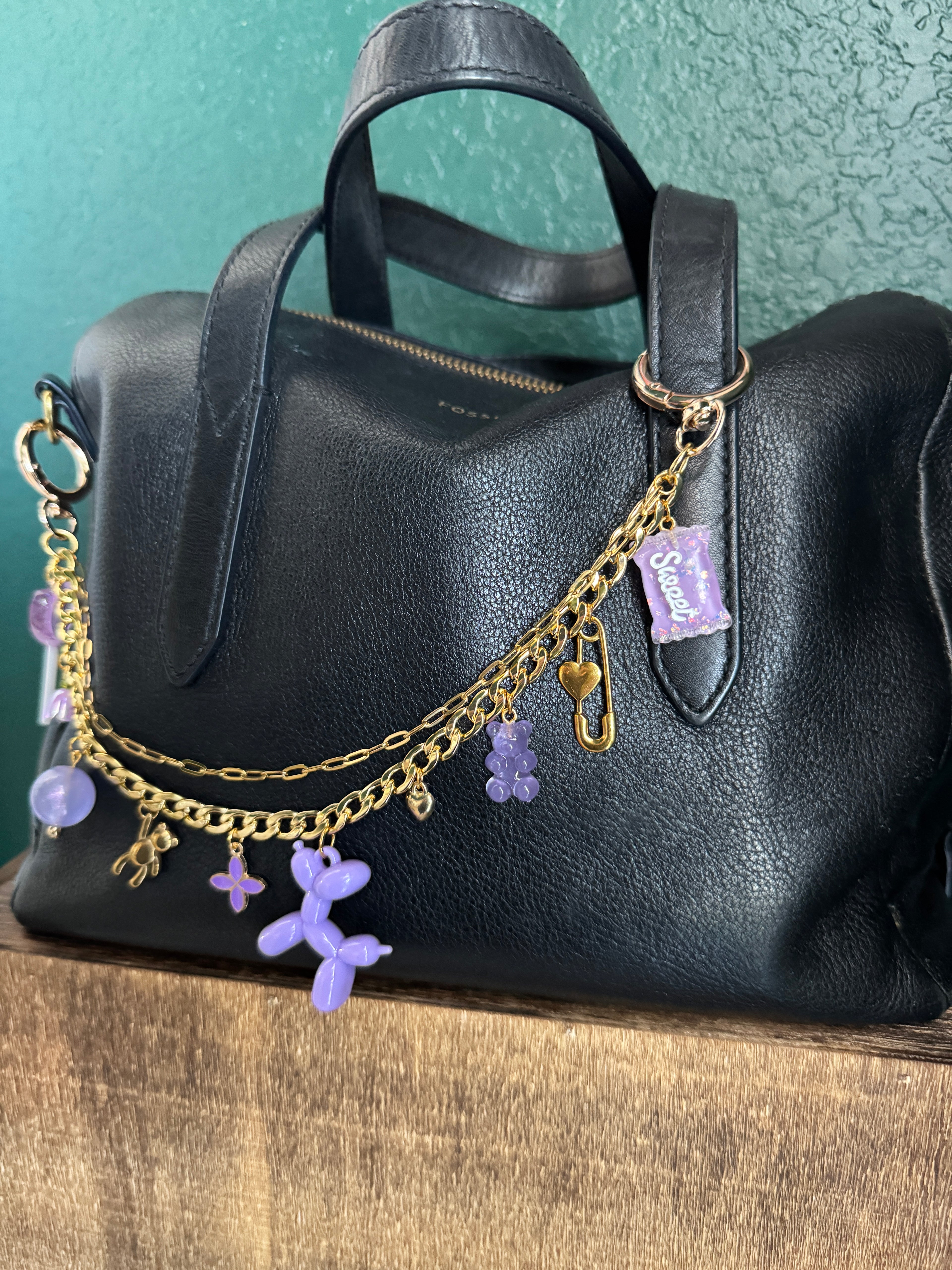 Black leather bag with gold chain and purple flowers on a textured surface