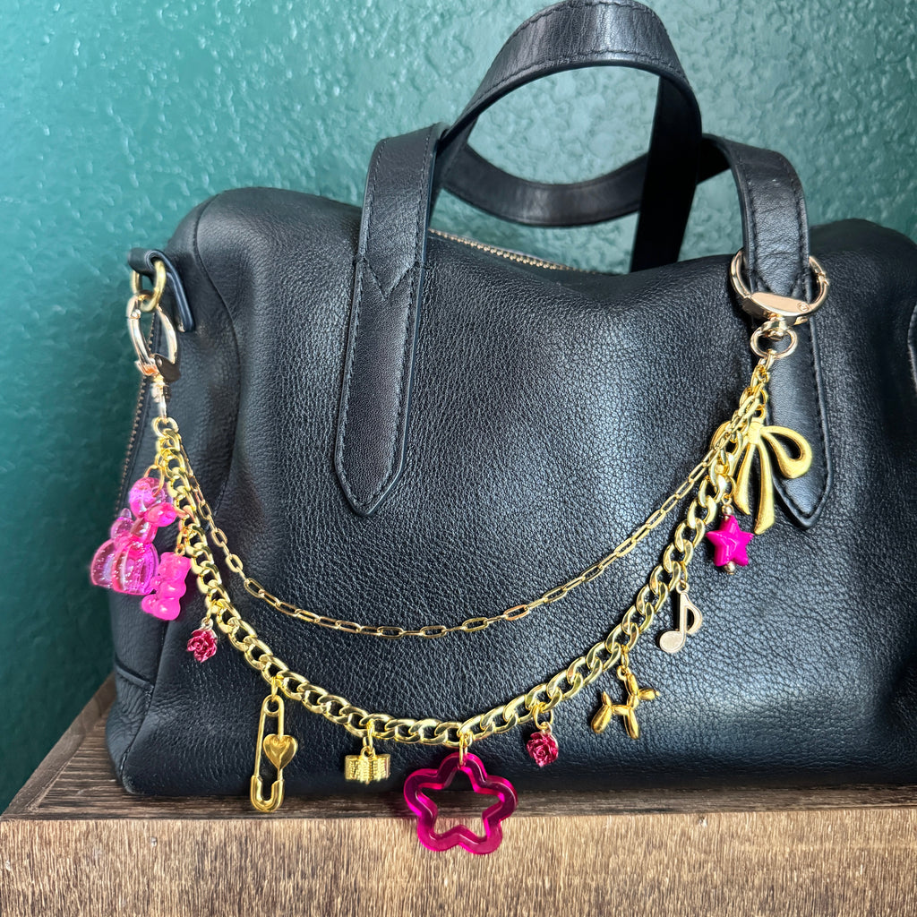 Black leather handbag with gold chain and pink floral charms on a wooden surface.