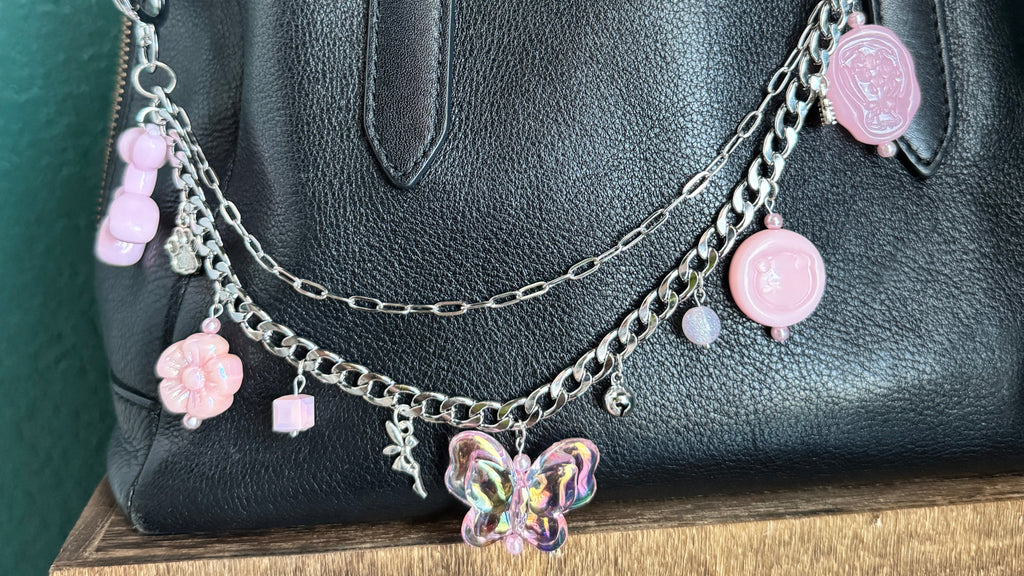 Black handbag with decorative pink and silver chain and charms on a green surface.