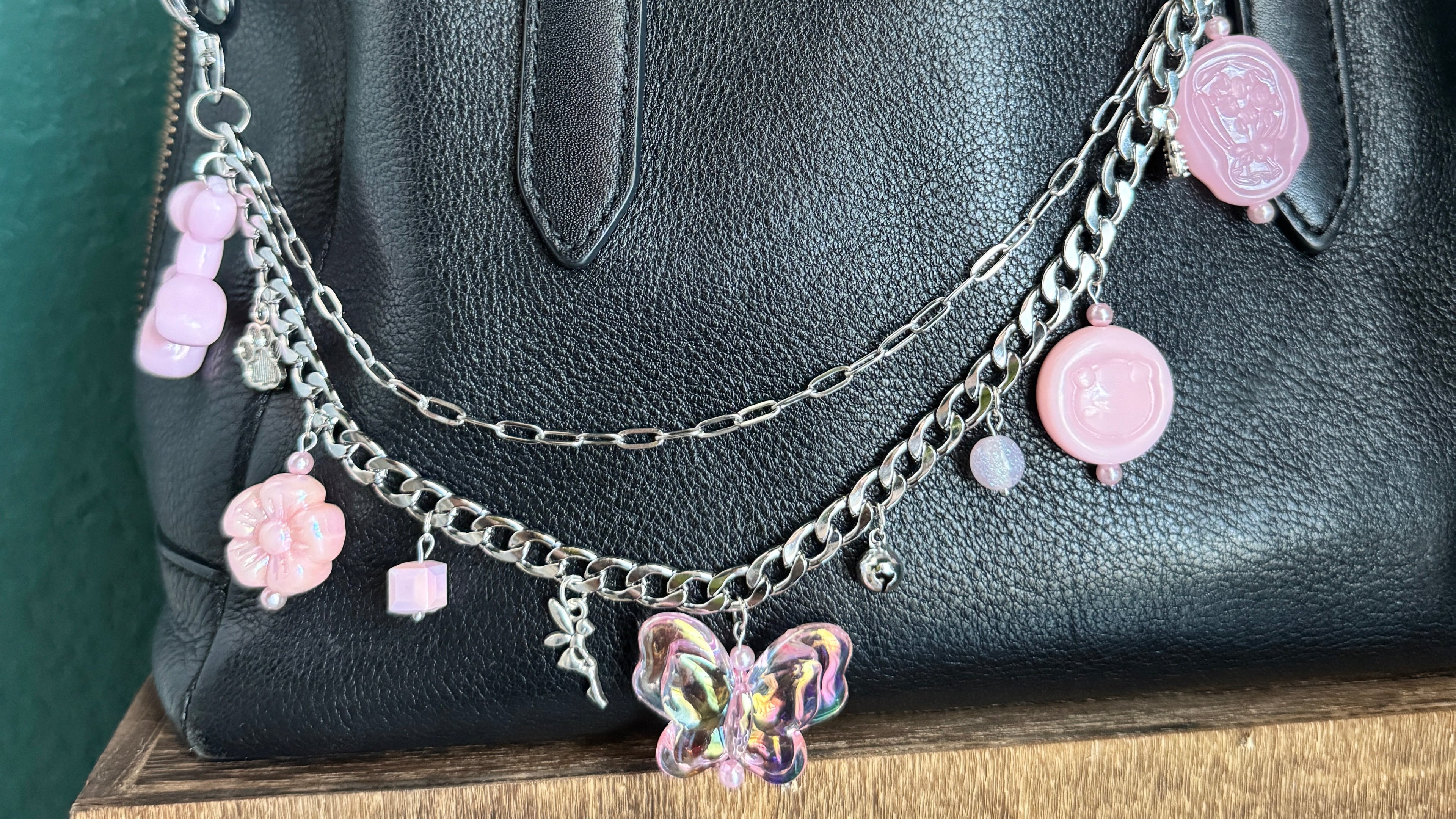 Black handbag with decorative pink and silver chain and charms on a green surface.