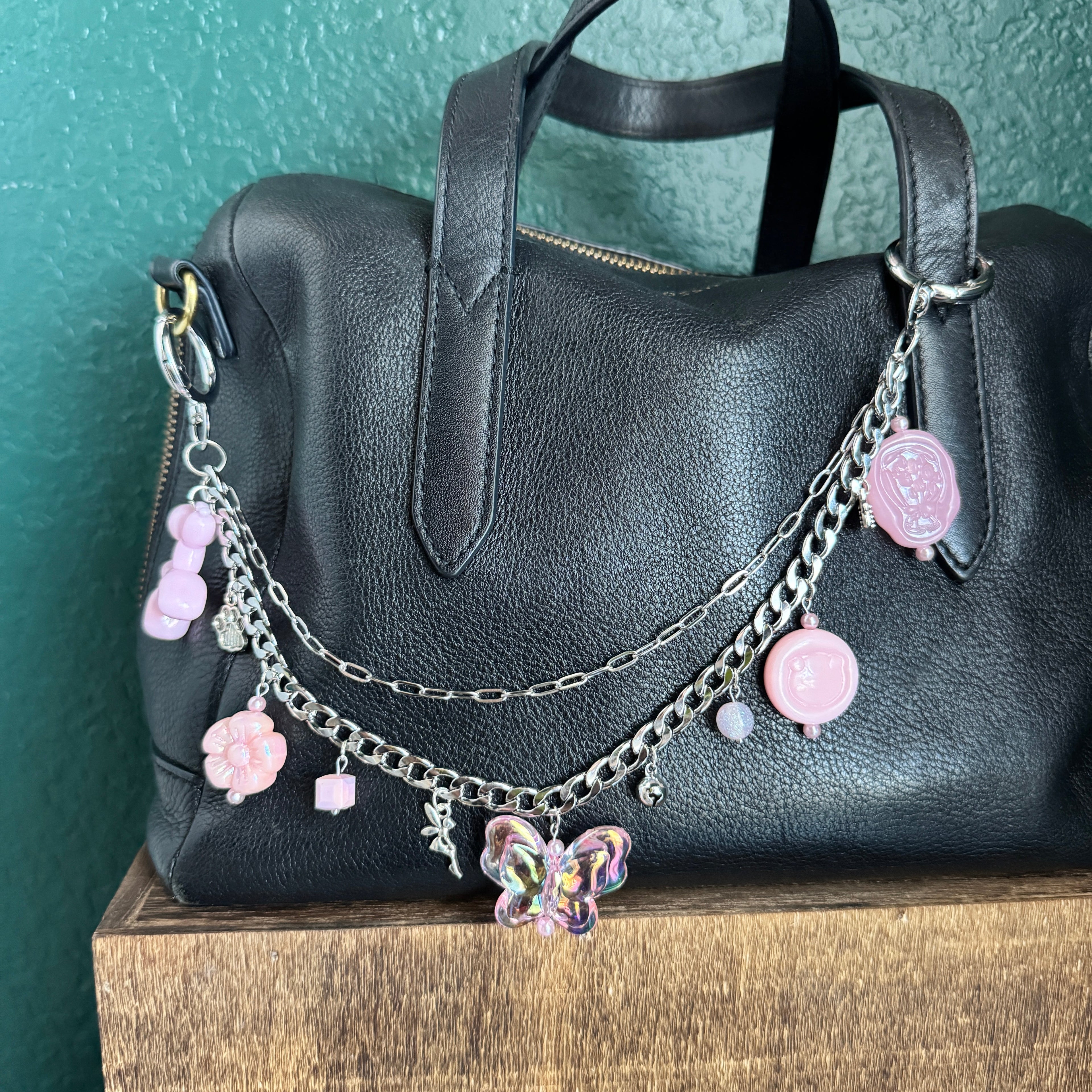 Black leather bag with decorative chain and charms on a green surface