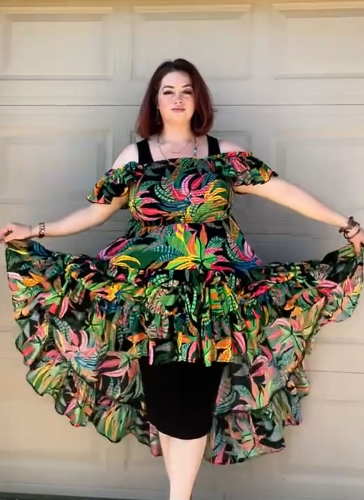 Woman wearing a colorful dress standing against a neutral wall.