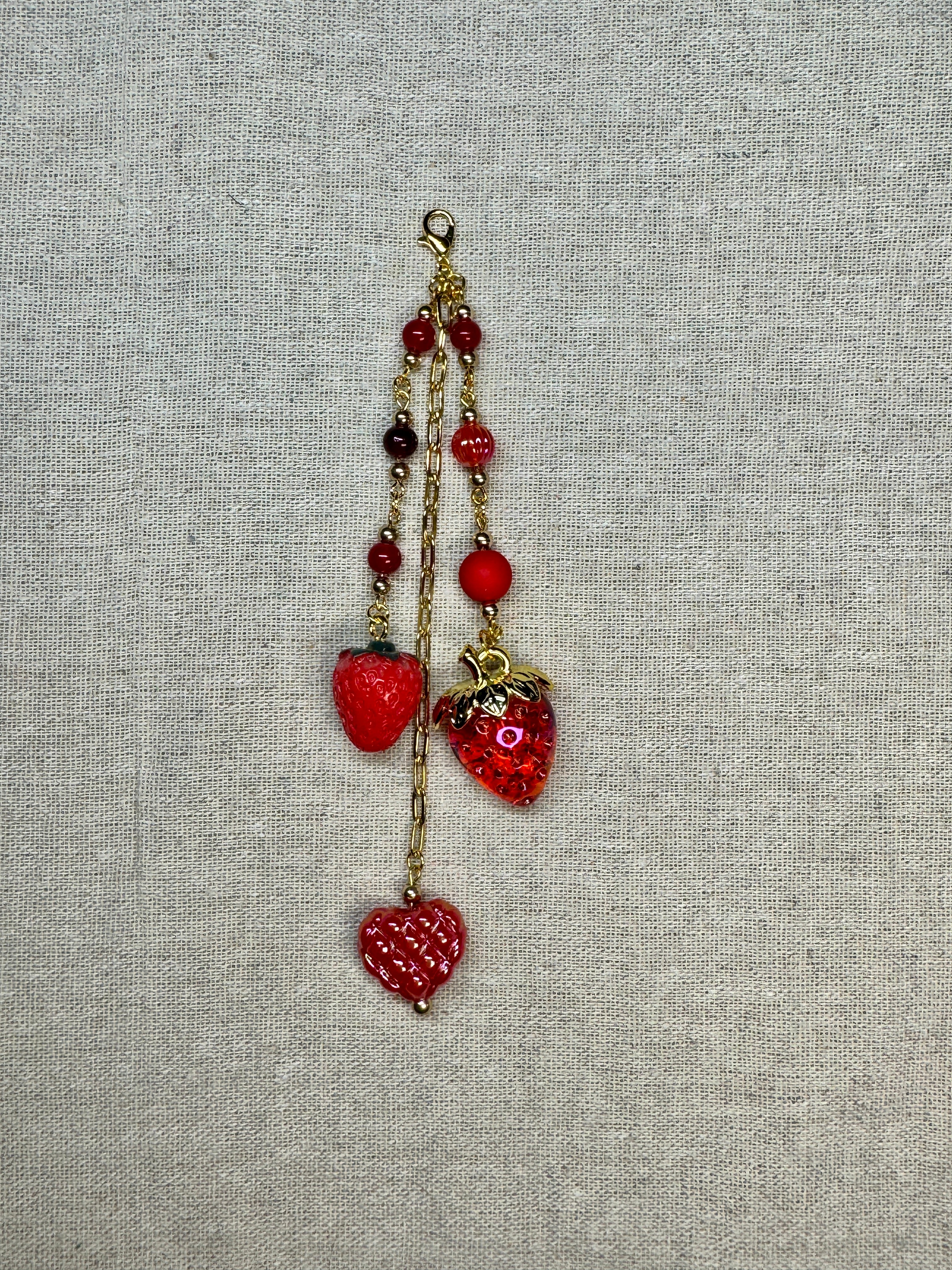 Red Strawberry shaped journal charm with red beads on a textured gray background