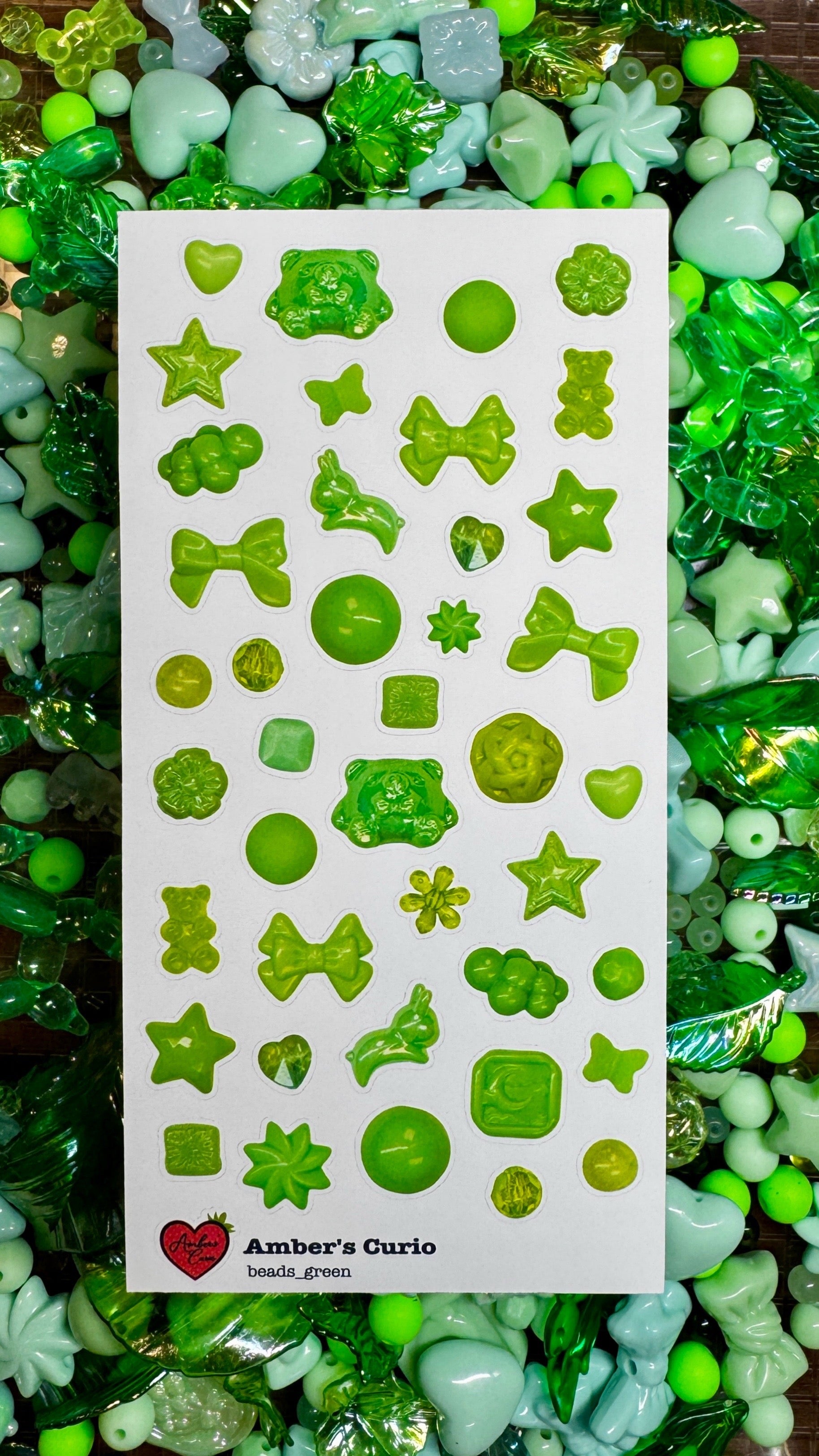 A sticker sheet of photographed green beads and charms printed on premium matte paper photographed on top of beads