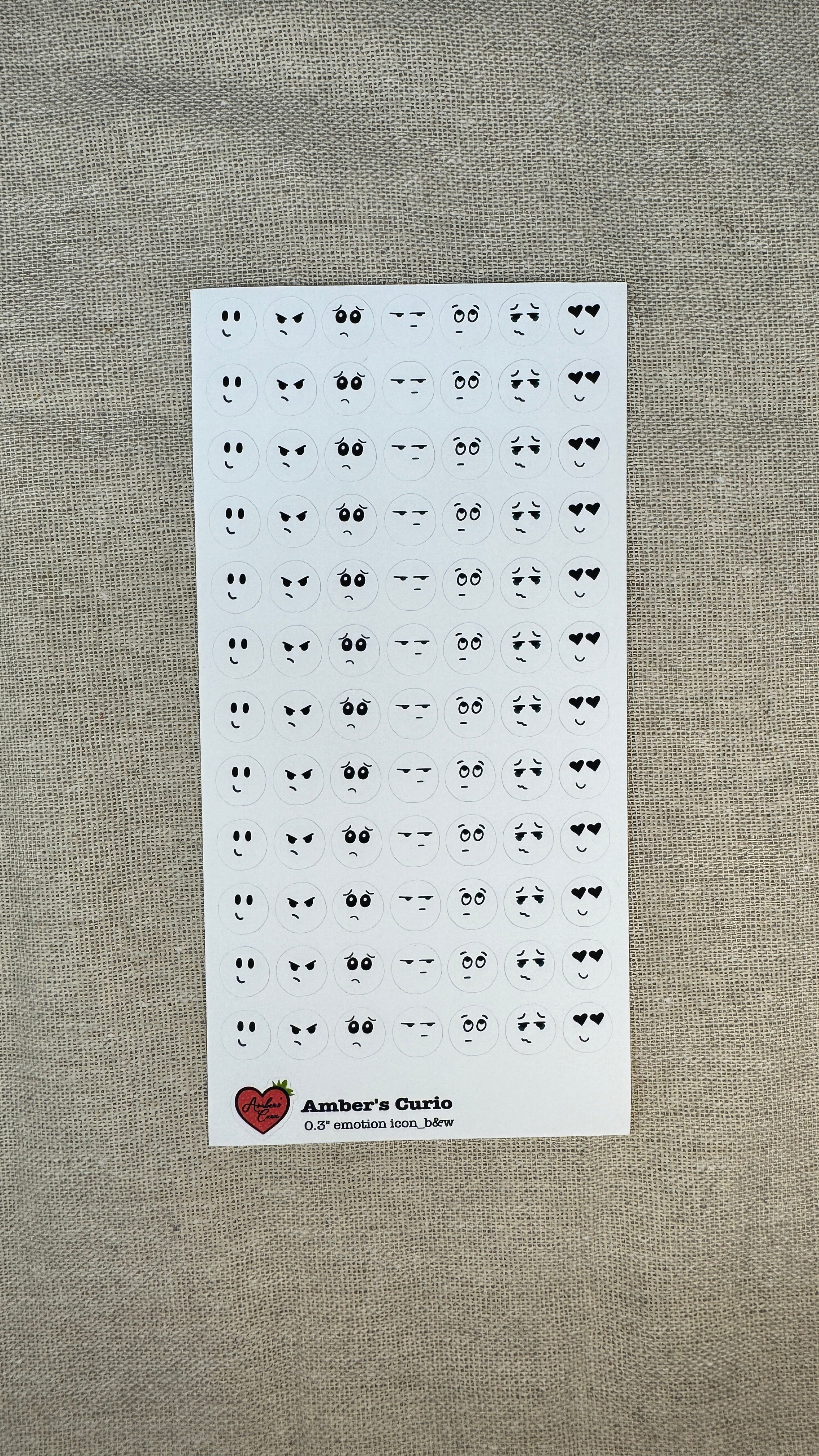 Sheet of small black and white emotion face stickers on a gray textured background