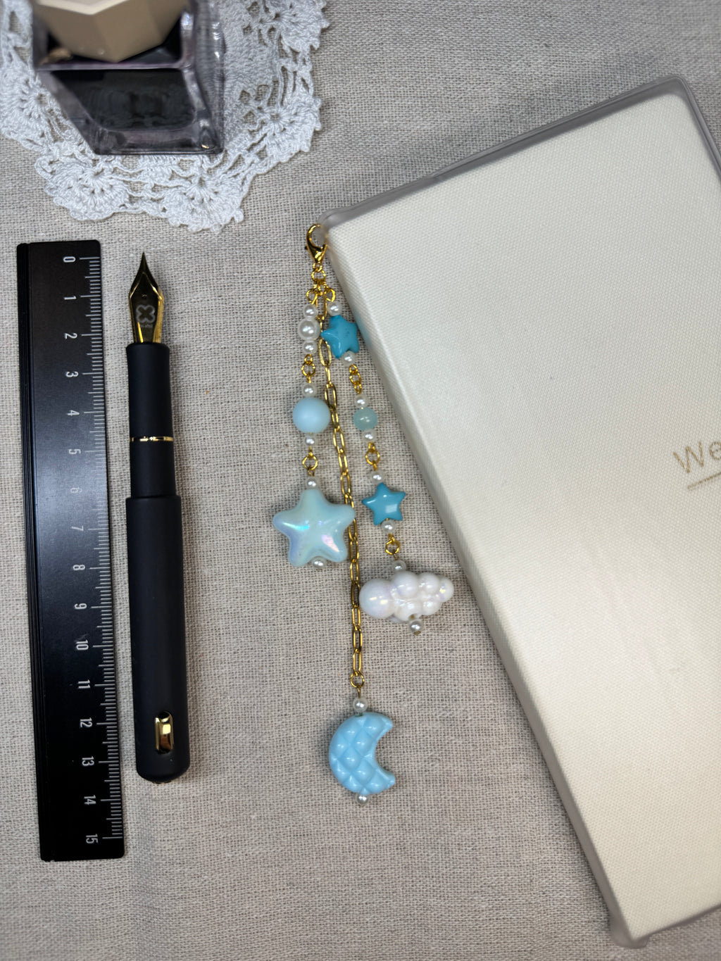 Decorative blue stars and clouds journal charm with a pen with charm on a textured surface next to a ruler and inkwell.