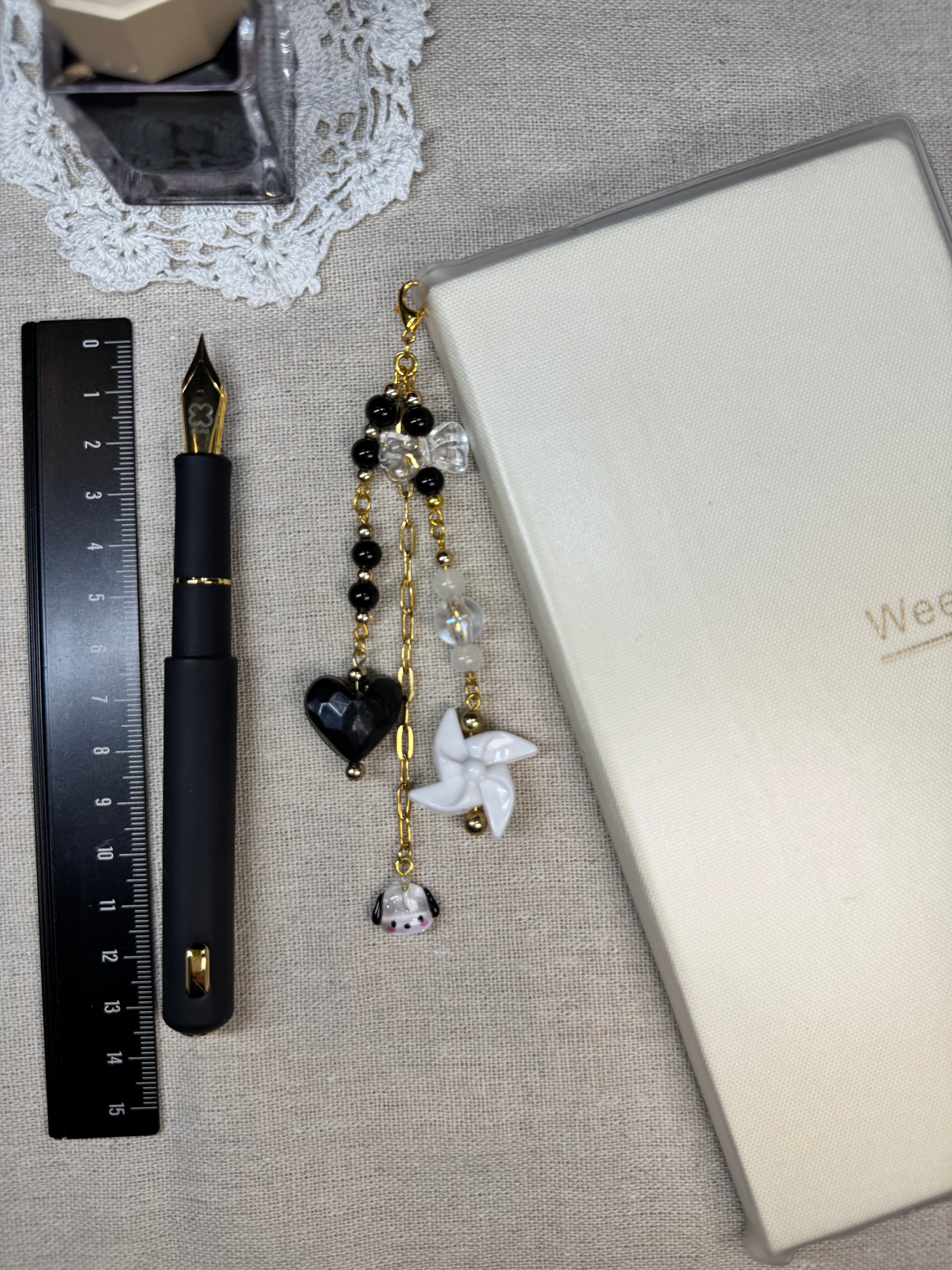 Journal charm with beads and gold accents on a linen with a pen and ruler.
