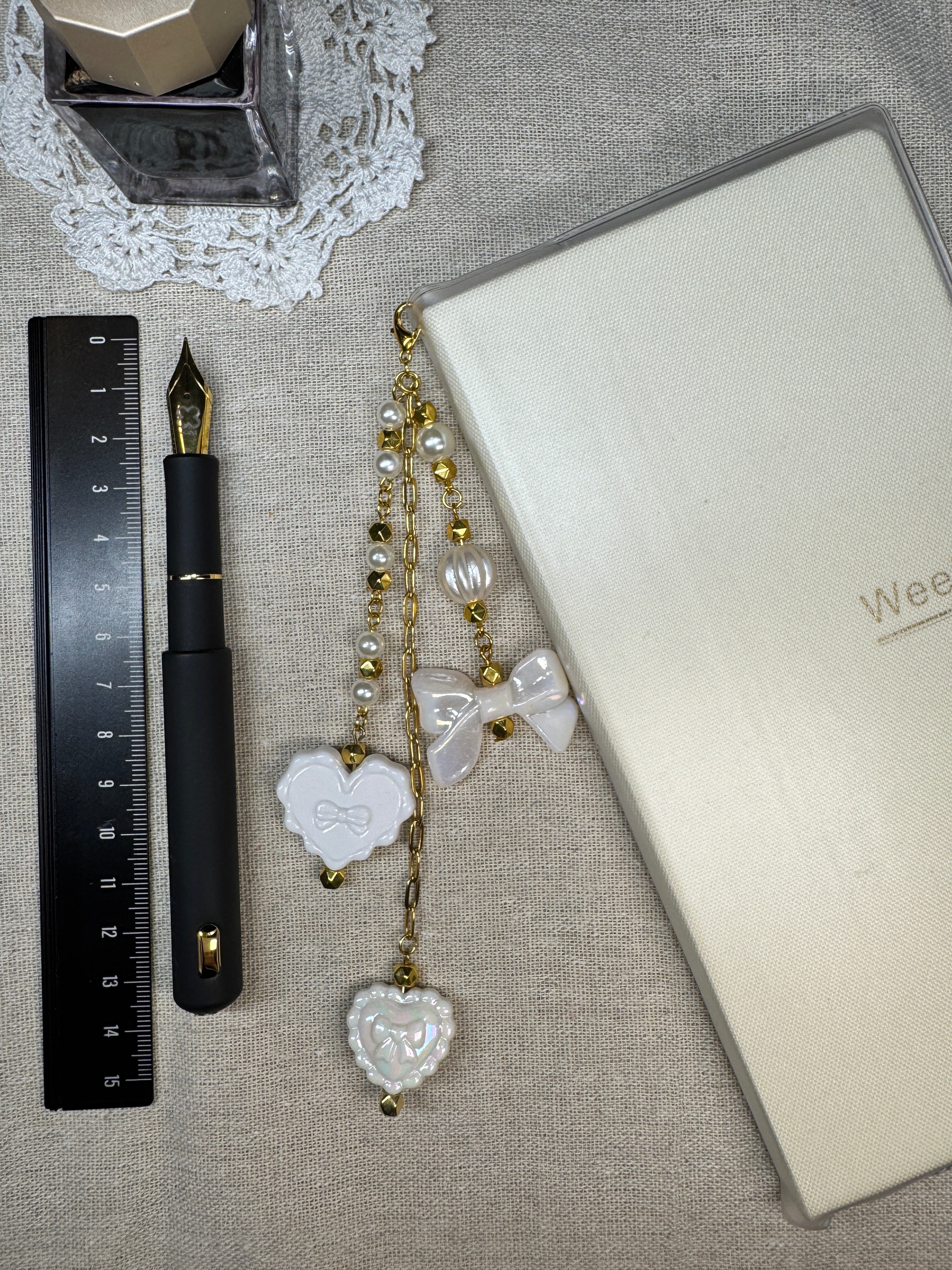 White journal charm next to fountain pen, and notebook on top of linen surface with a ruler for scale.
