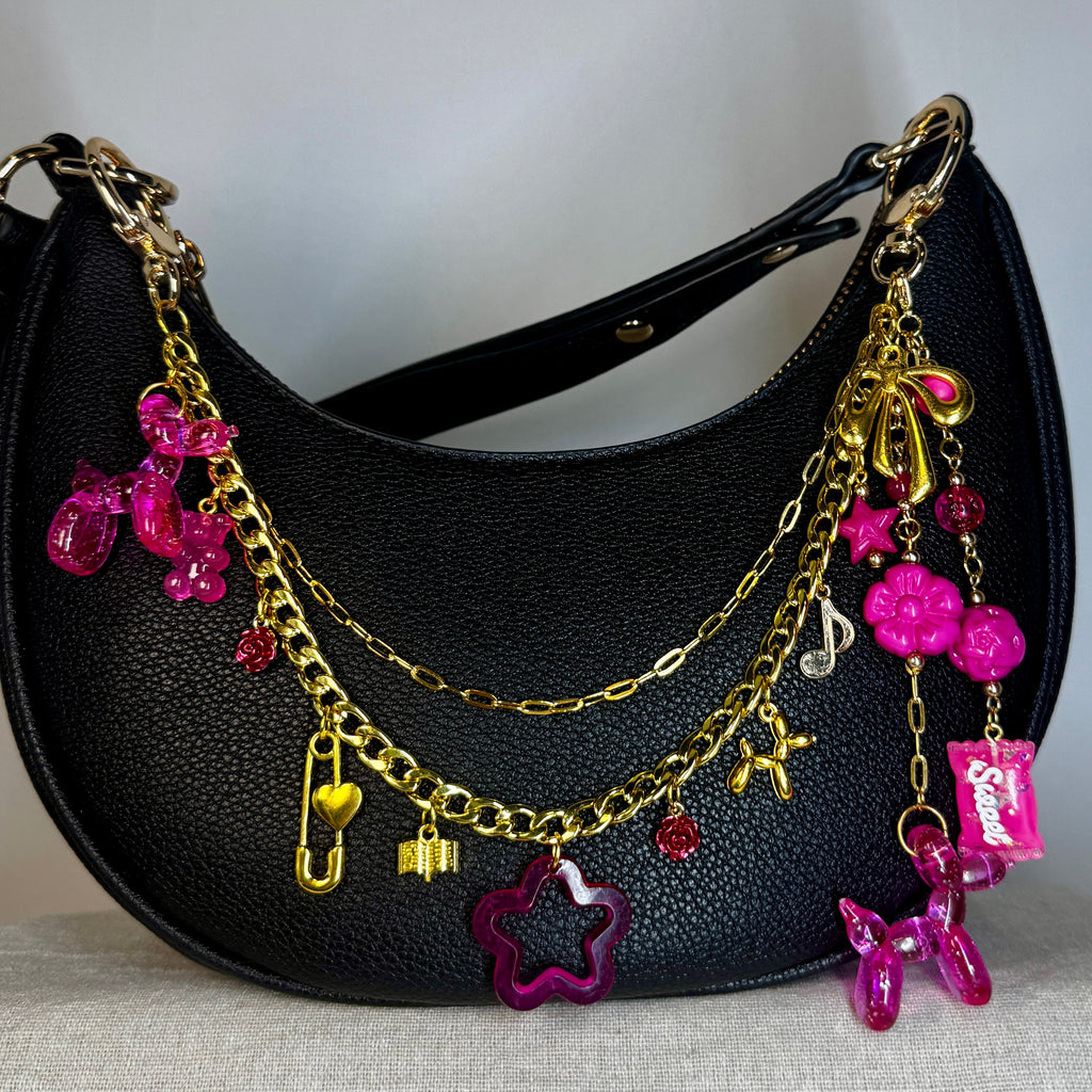 Black handbag with gold and pink charms on a light gray background