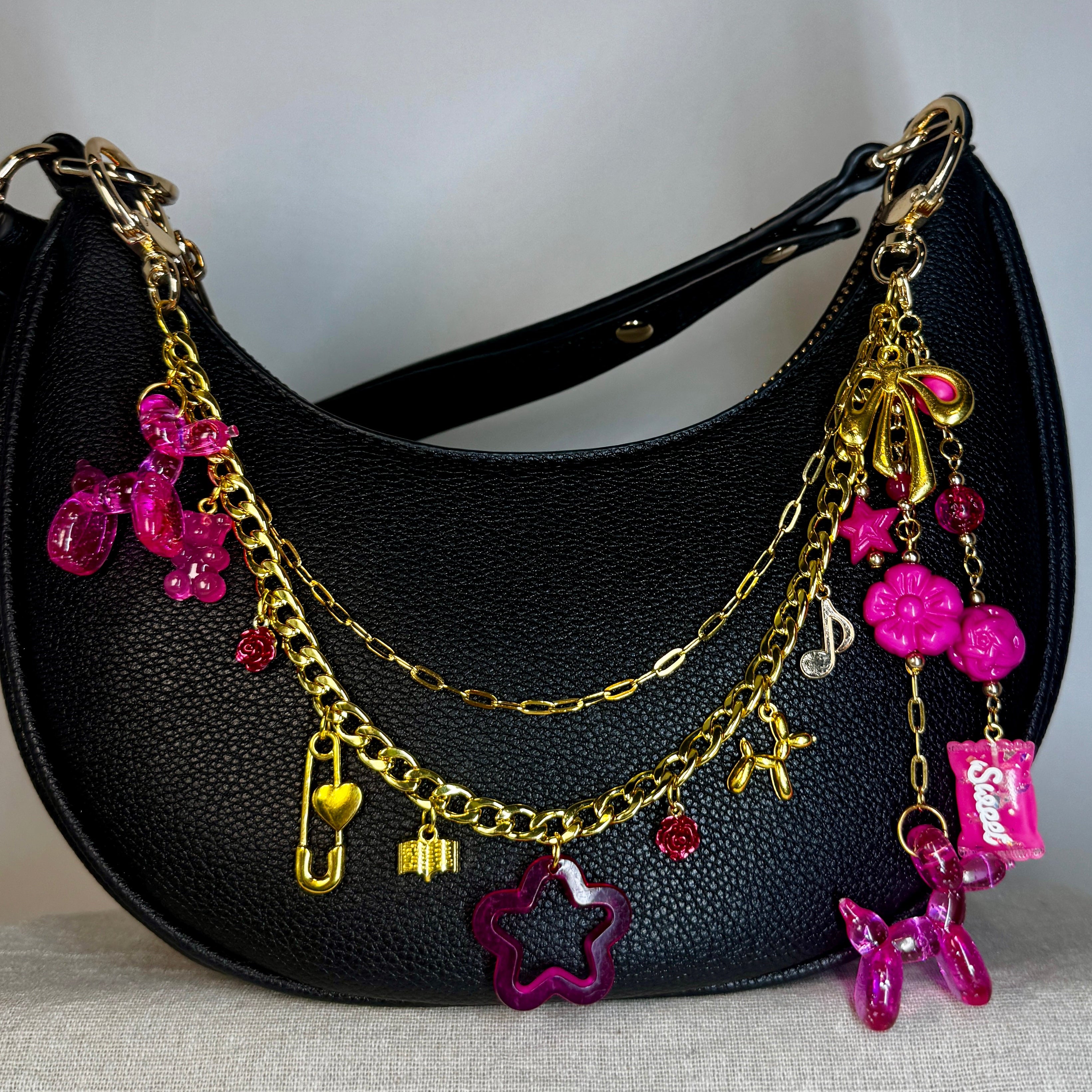 Black handbag with gold and pink charms on a light gray background