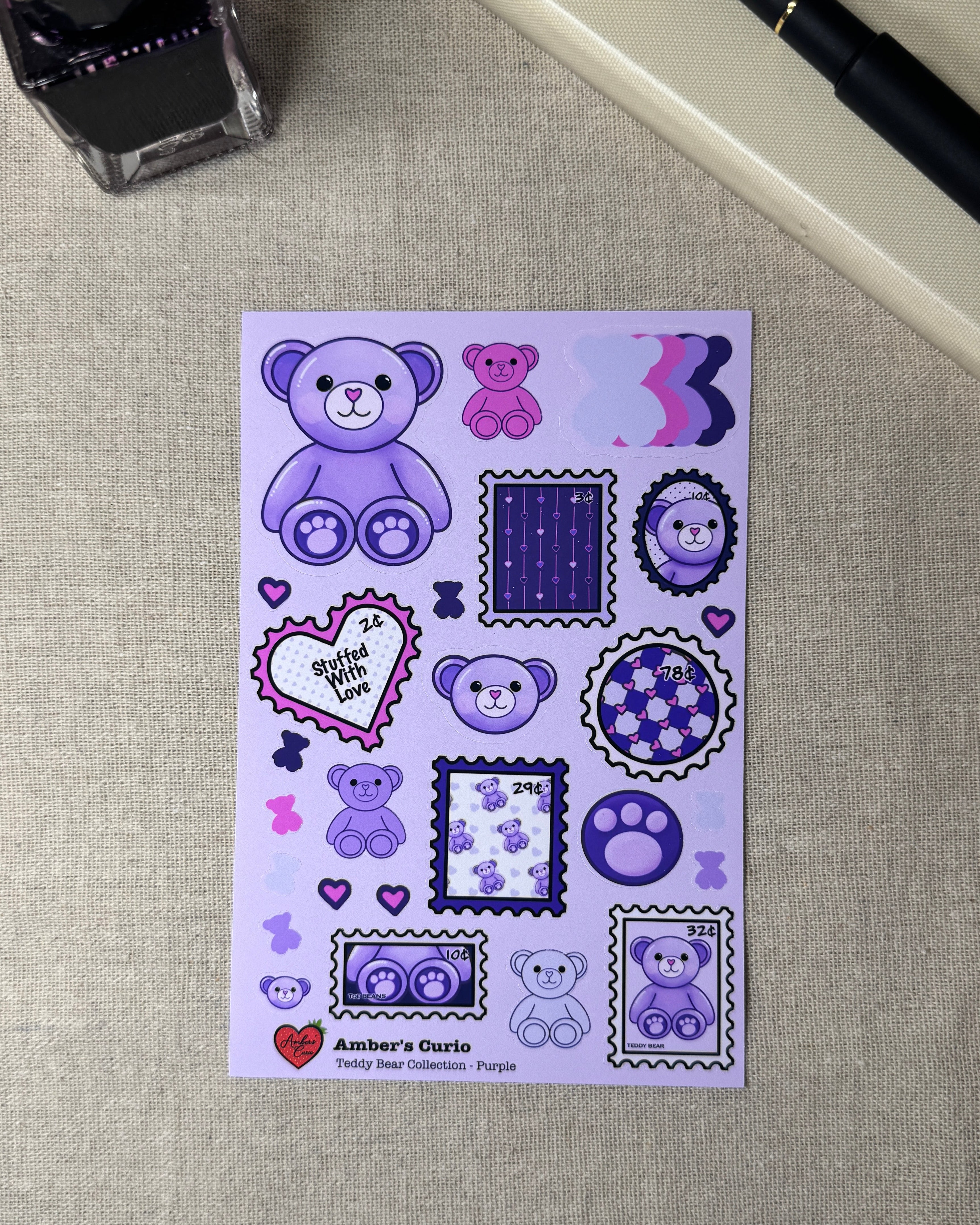 Sticker sheet of a teddy bear within stamp shapes and kawaii themed doodles next to a journal fountain pink and an ink bottle. 